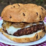 A French onion soup burger on a plate, with provolone, swiss, and caramelized onions.