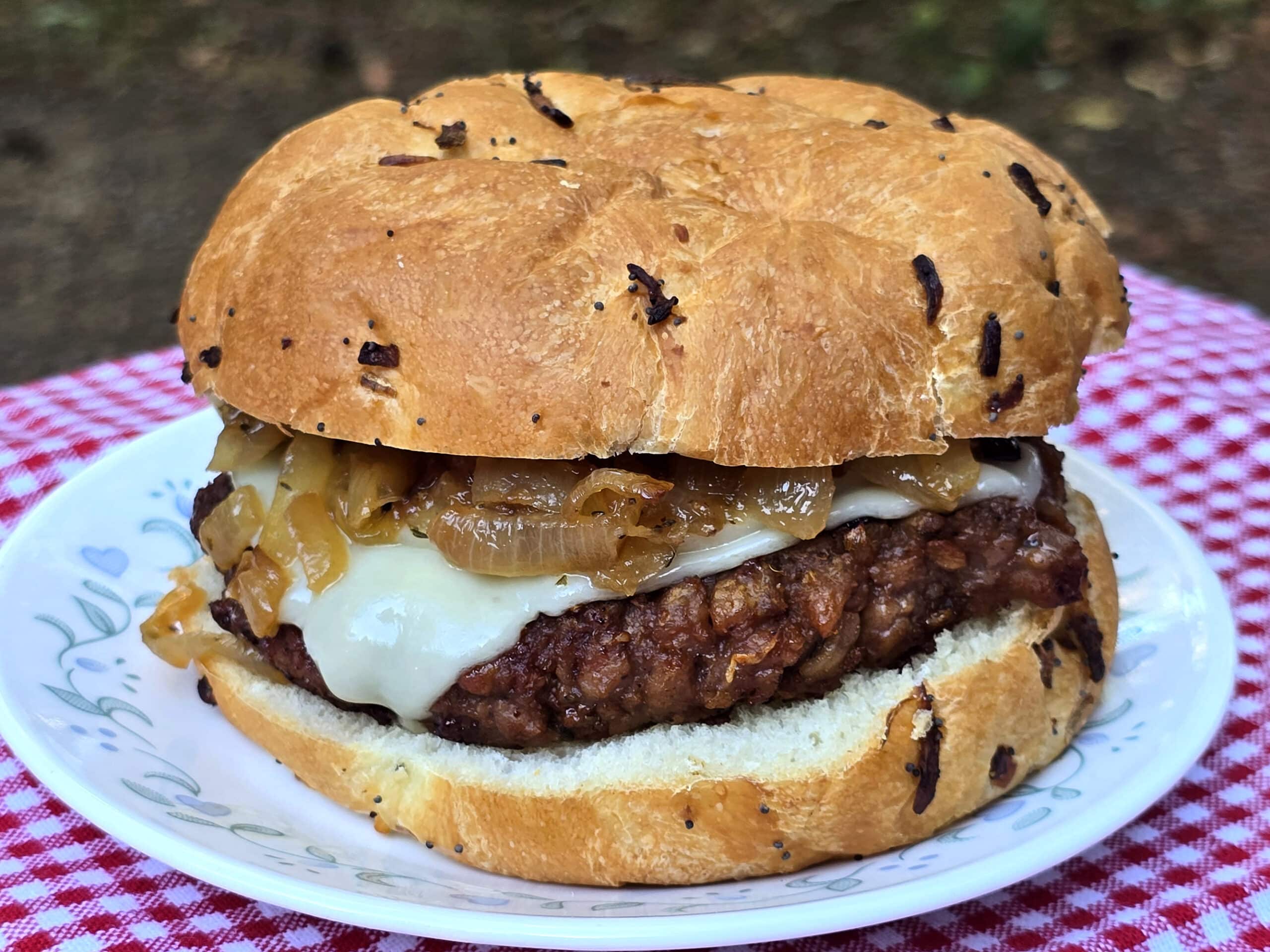 A French onion soup burger on a plate, with provolone, swiss, and caramelized onions.