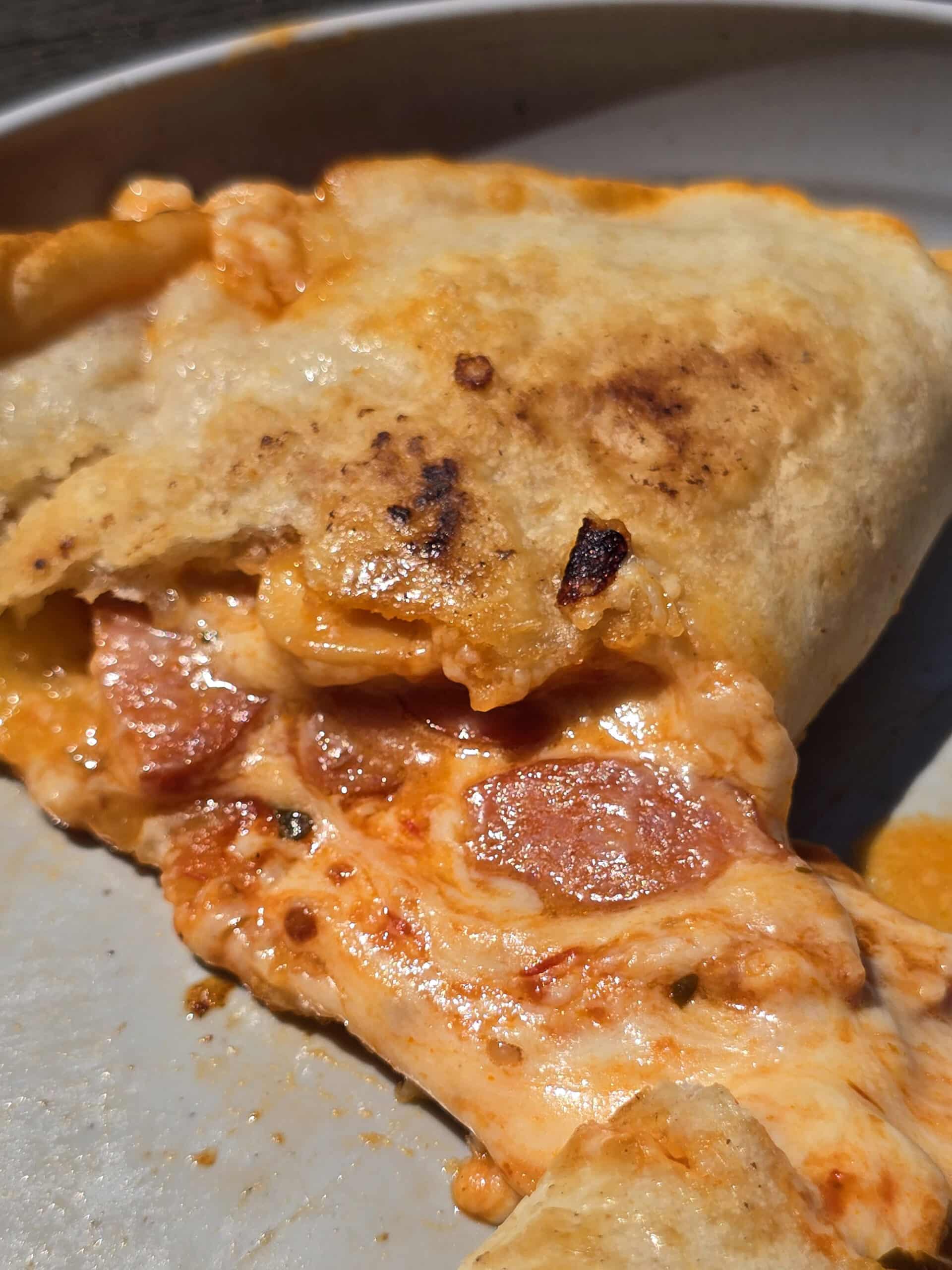 A grilled calzone on a plate.  It's split in half to show the pizza filling.