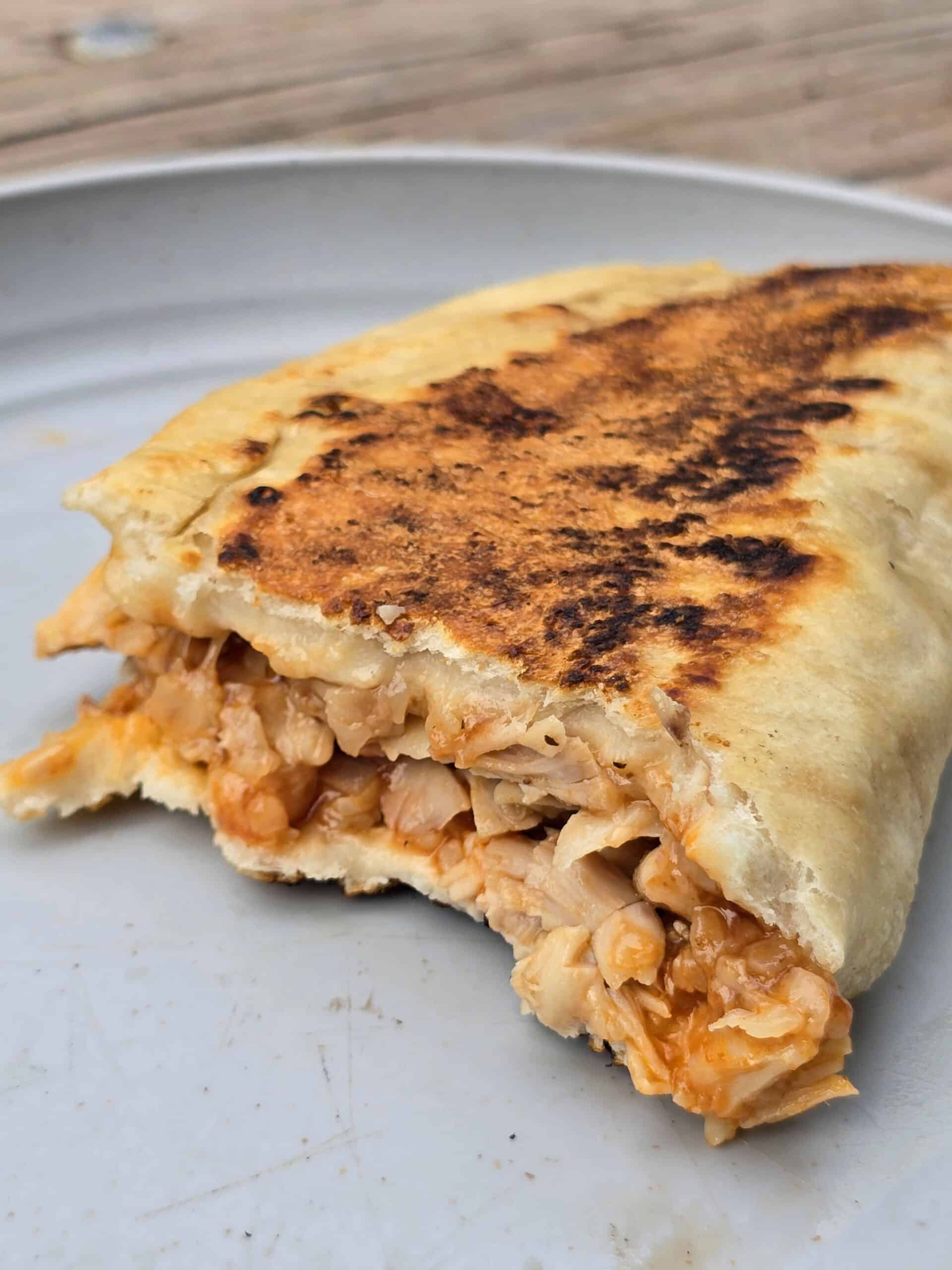 A grilled calzone on a plate.  It’s split in half to show the BBQ chicken filling.