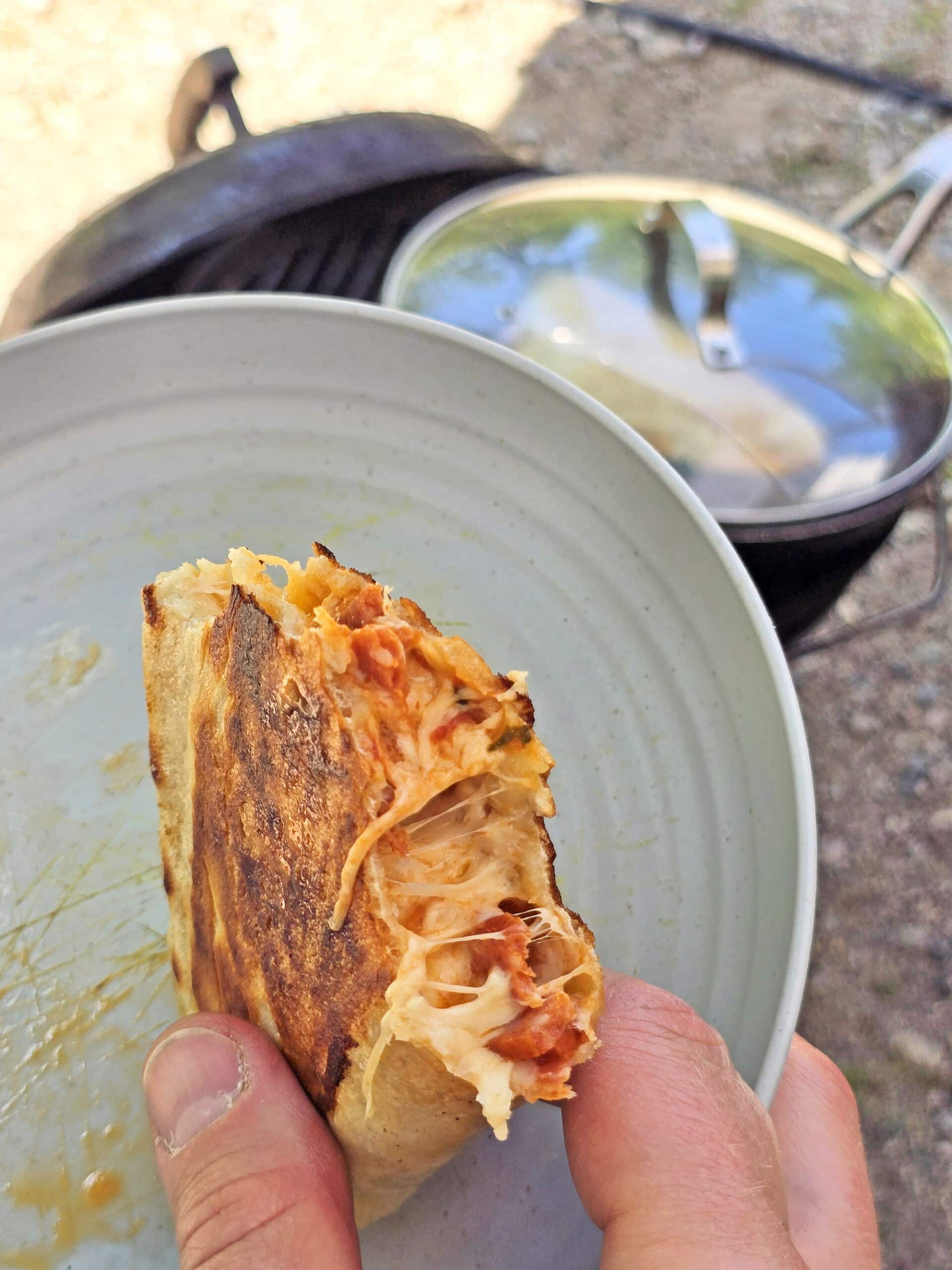 A half eaten pizza filled campfire calzone being held over a plate.
