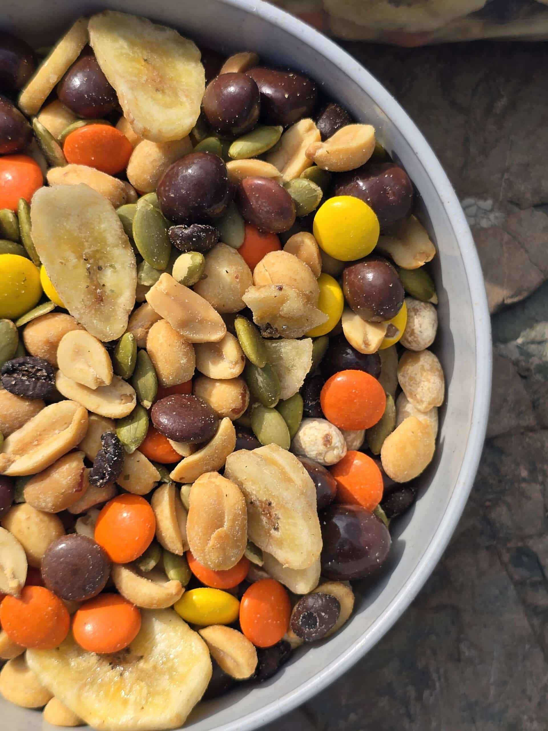 A bowl of caffeinated trail mix with reeses pieces, chocolate covered coffee beans, pepitas, peanuts, and dried banana chips.