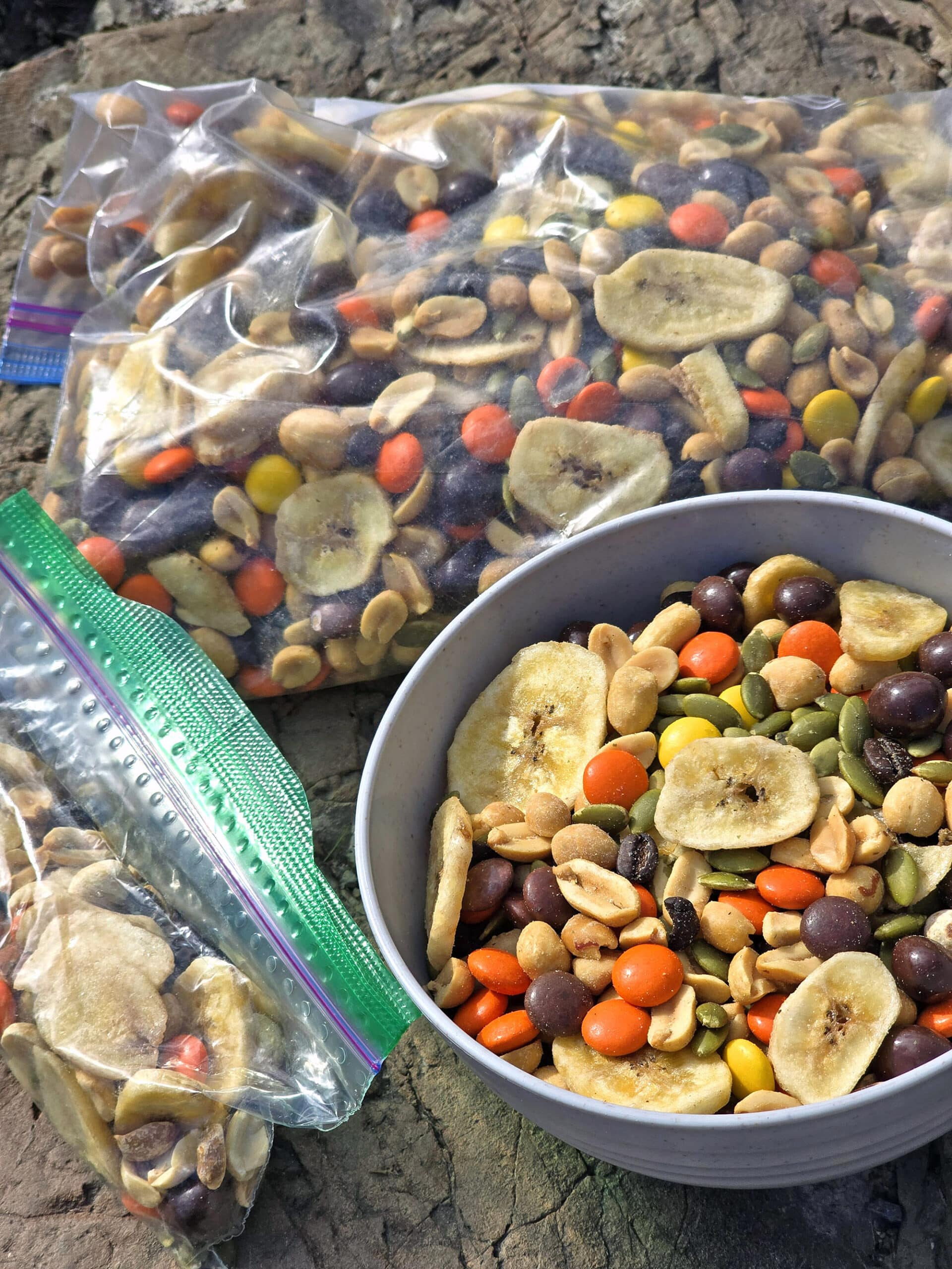 A bowl and bag of caffeinated trail mix with reeses pieces, chocolate covered coffee beans, pepitas, peanuts, and dried banana chips.