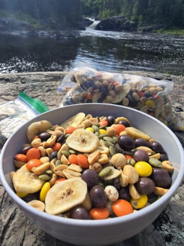 A bowl and bag of caffeinated trail mix with reeses pieces, chocolate covered coffee beans, pepitas, peanuts, and dried banana chips.
