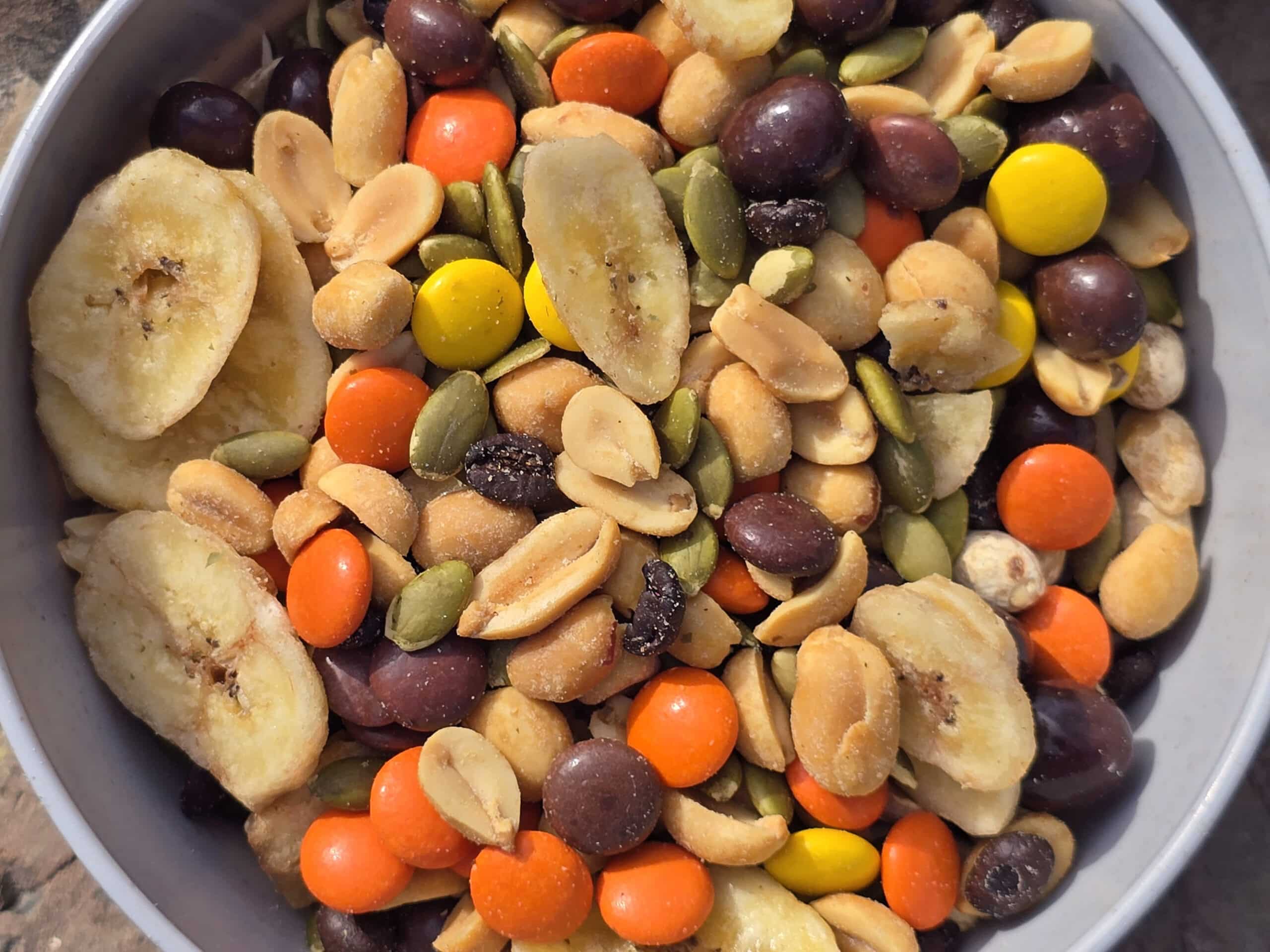 A bowl of caffeinated trail mix with reeses pieces, chocolate covered coffee beans, pepitas, peanuts, and dried banana chips.