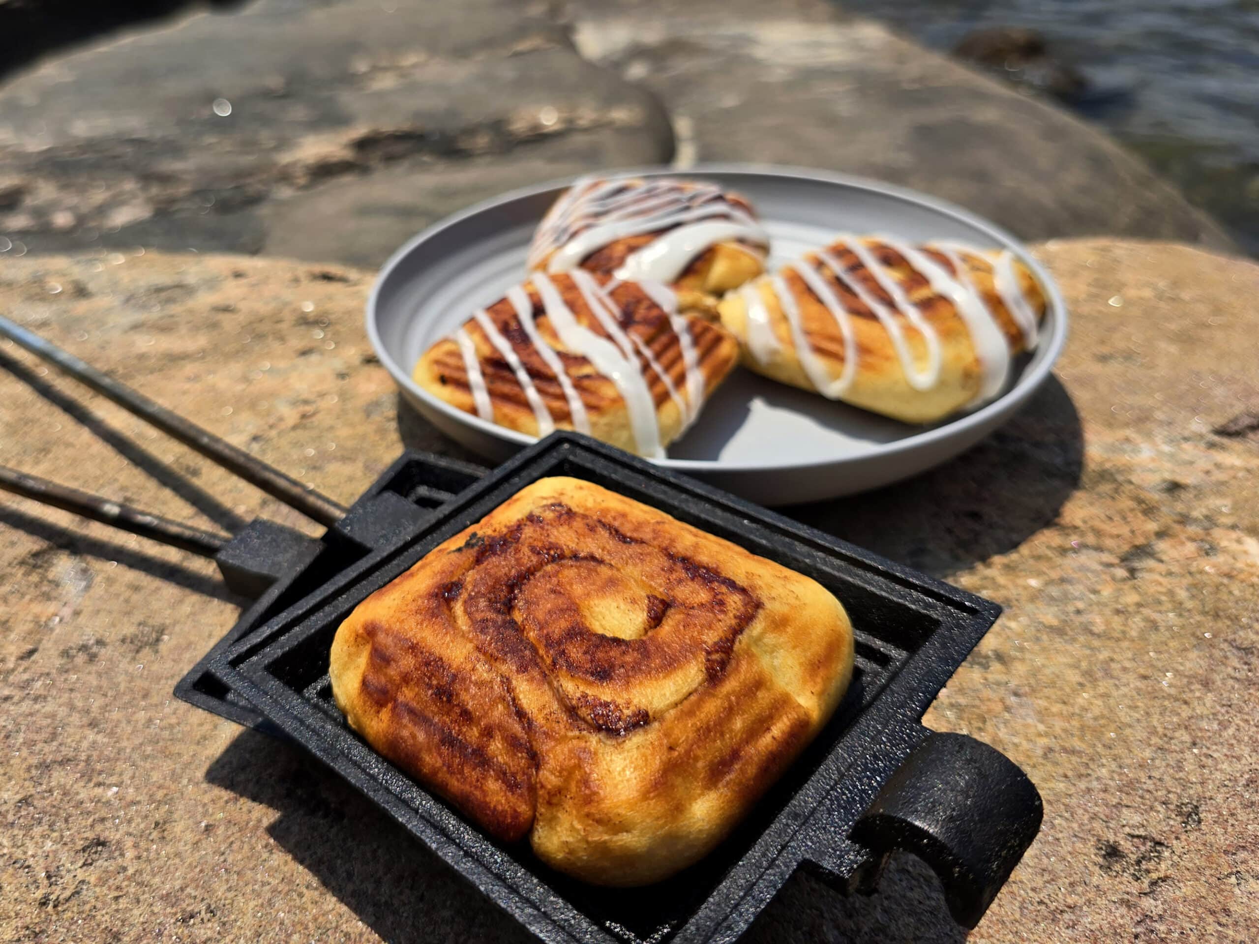 A plate of frosted pie iron cinnamon buns and an unfrosted cinnamon bun in a pie iron.