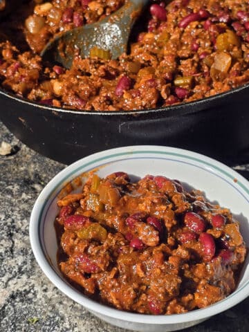 A pan and bowl of smoky venison chili with beans and chunky vegetables visible.