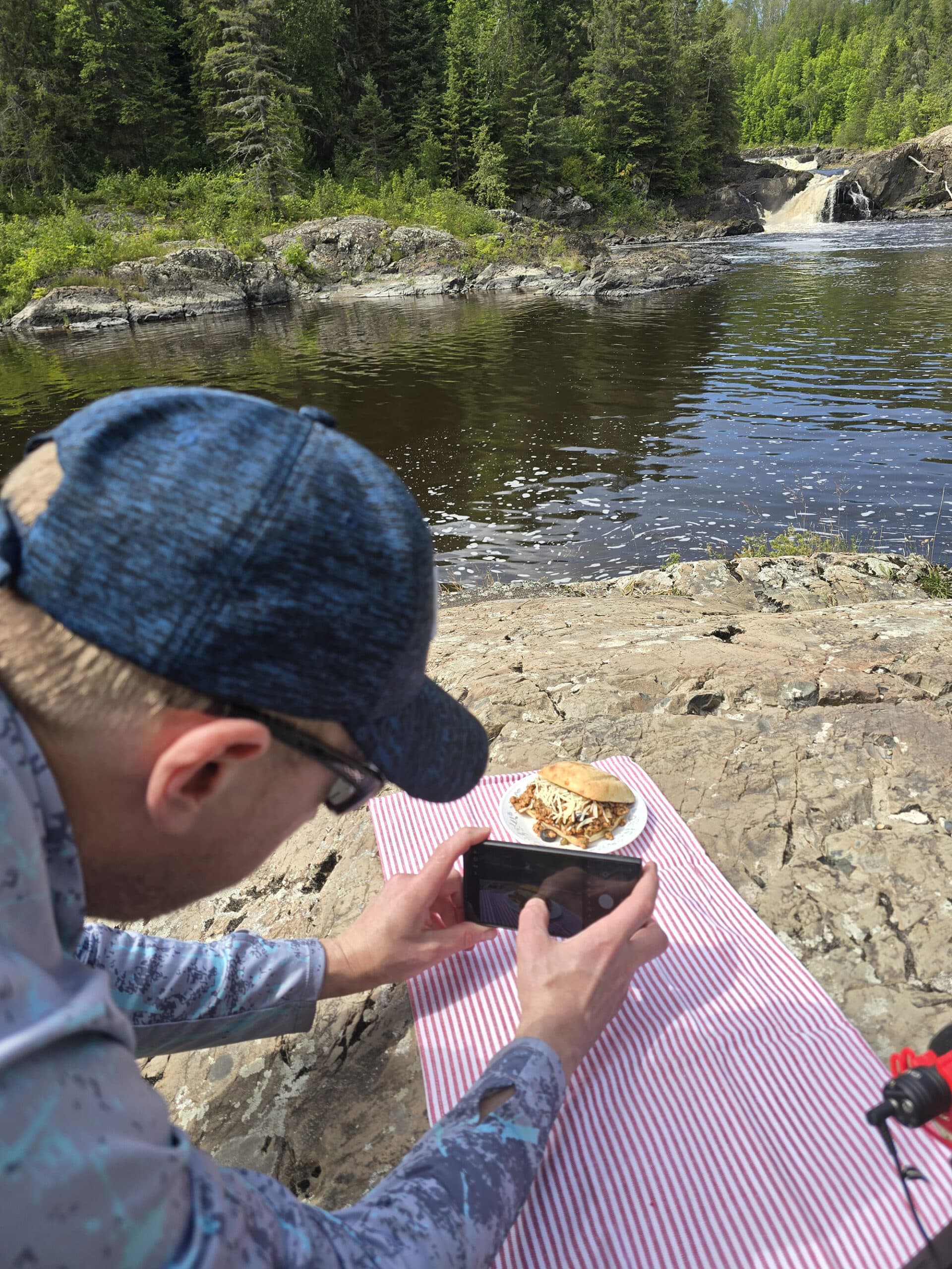A man photographing puttanesca sloppy joes in front of a river and waterfall.