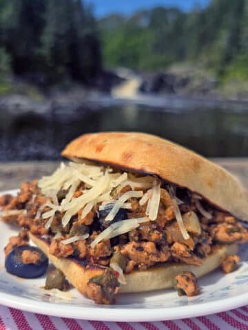 A Puttanesca sloppy joe on a ciabatta roll with black olives, capers, and parmesan cheese visible.