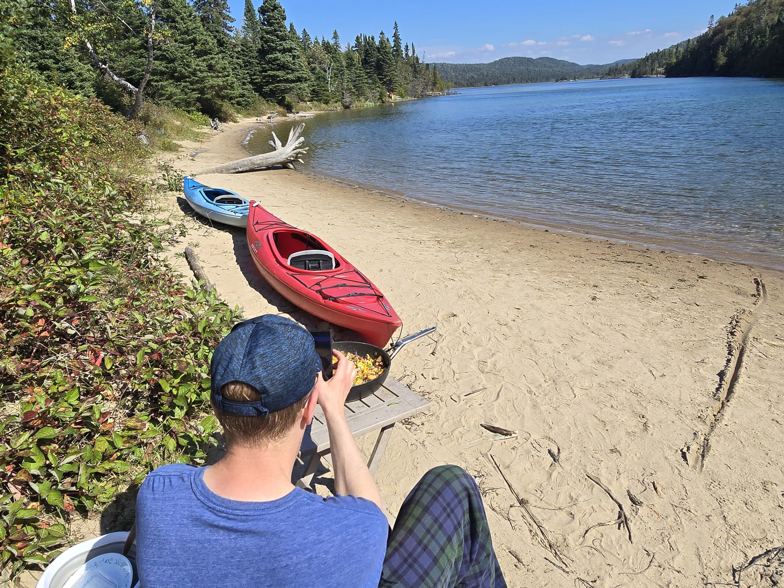 A man photographing chipotle breakfast hash on a beach with kayaks on it.