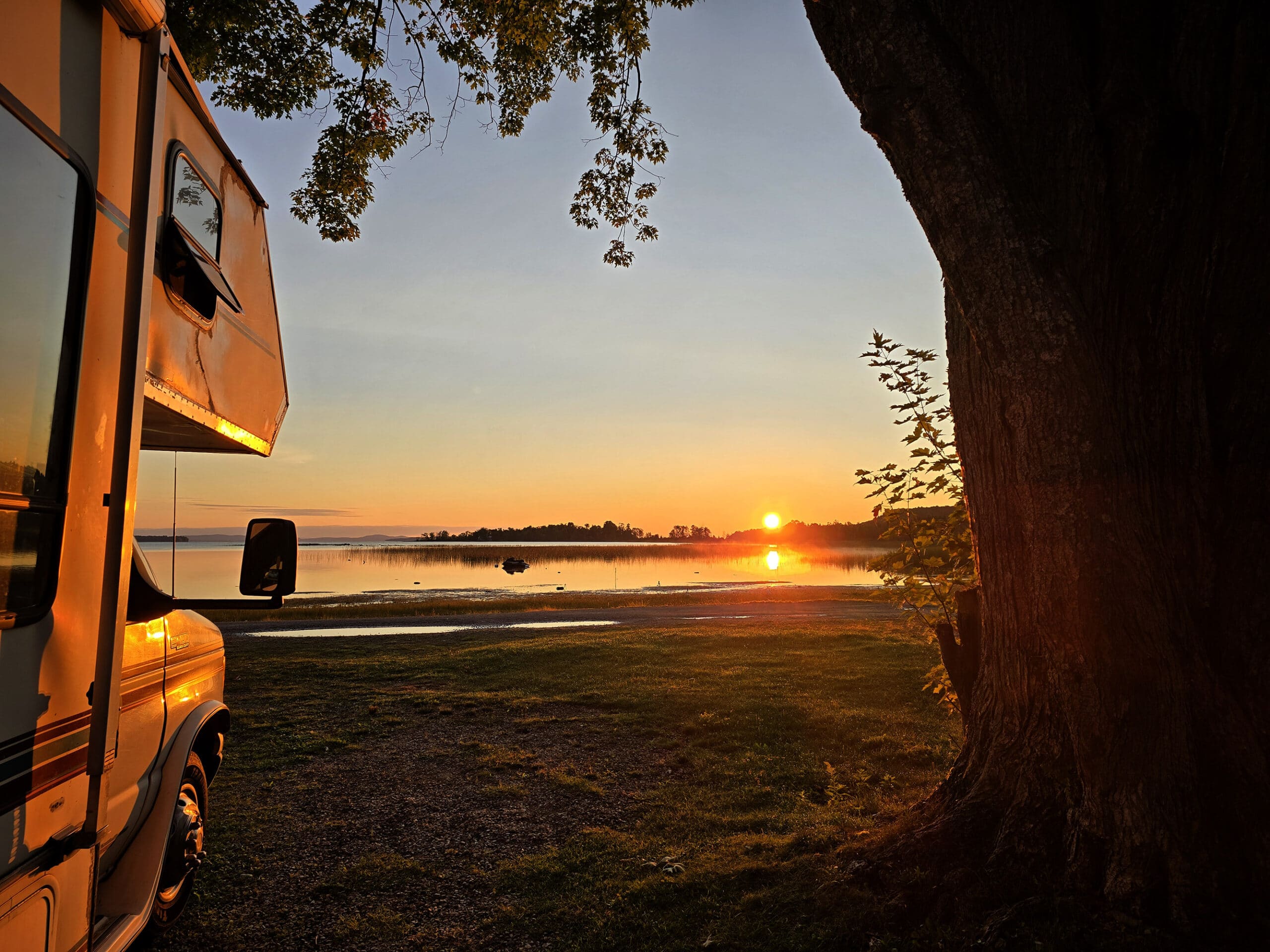 A sunrise with an rv and a tree in the foreground.