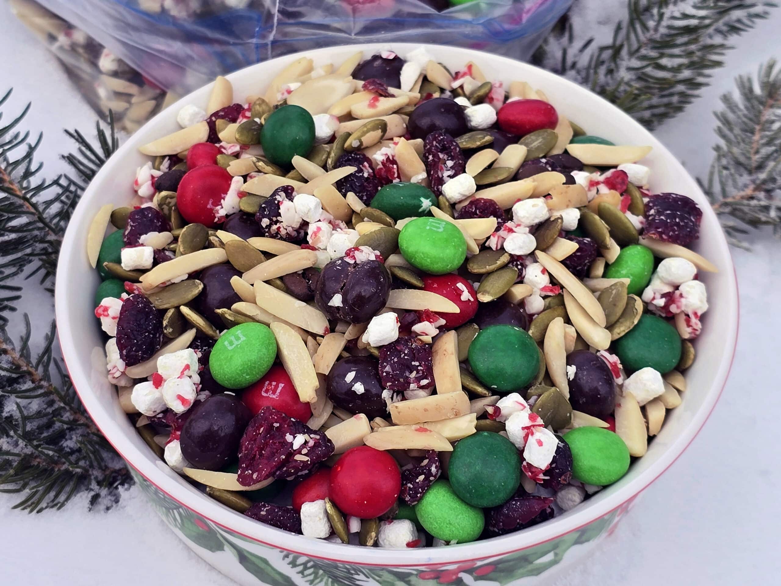 A bowl and a large plastic baggie of Christmas snack mix in the snow.