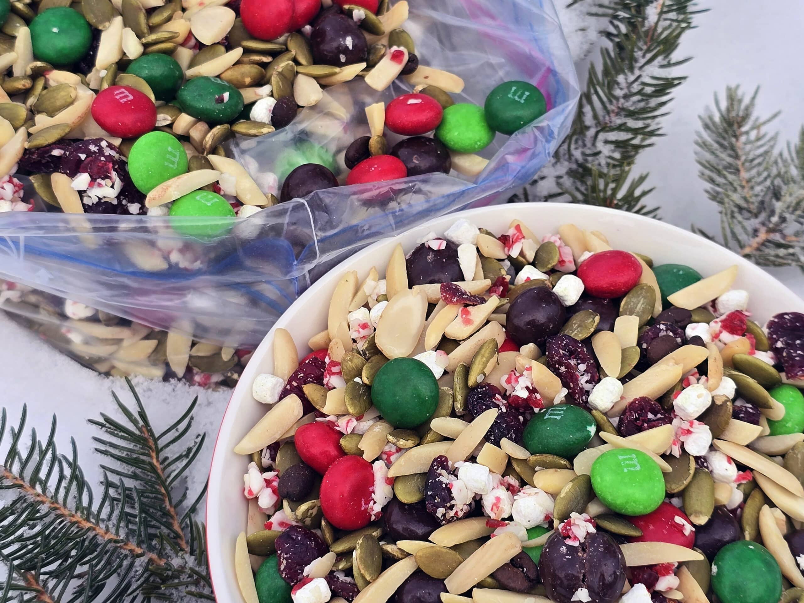 A bowl and a large plastic baggie of Christmas trail mix in the snow.