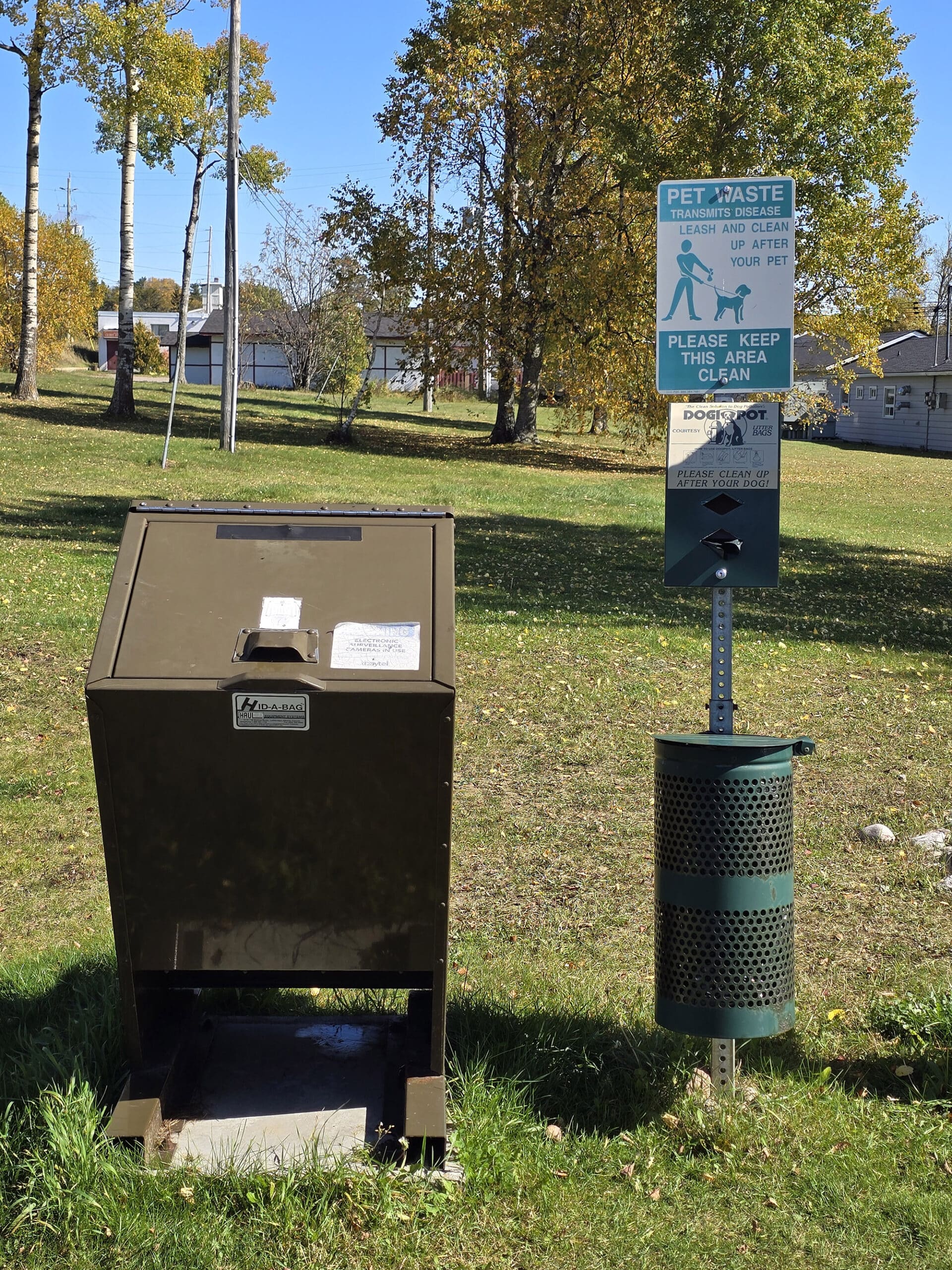 A garbage can next to a dog poop baggie dispenser.
