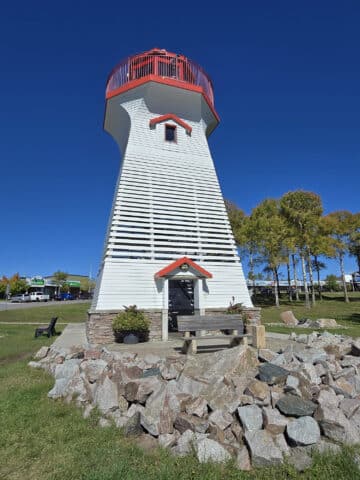 The terrace bay lighthouse, with mounded rocks in front and lawn all around it.
