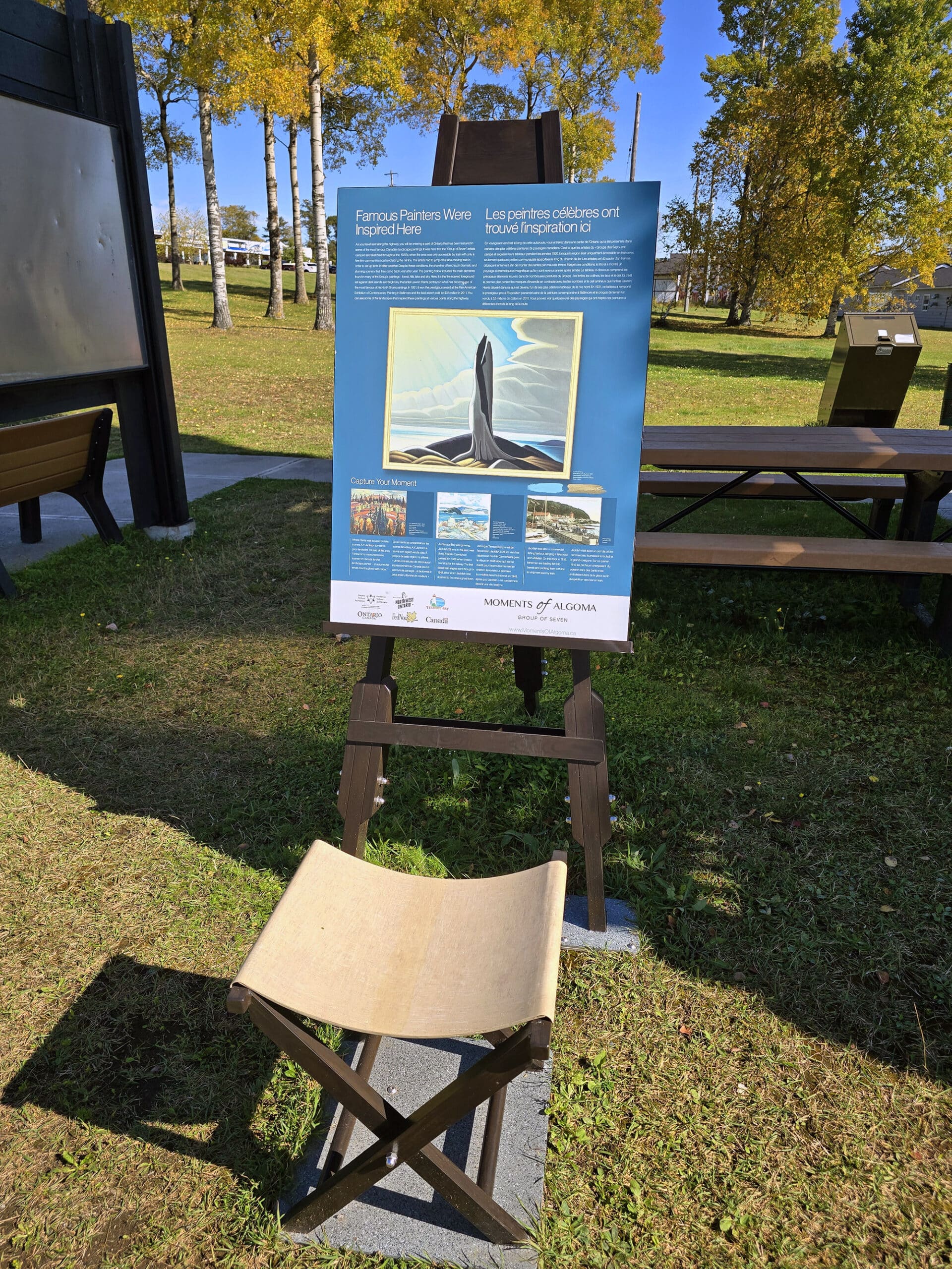 A Moments of Algoma display, with educational signage mounted on an easel, with an artists chair in front of it.