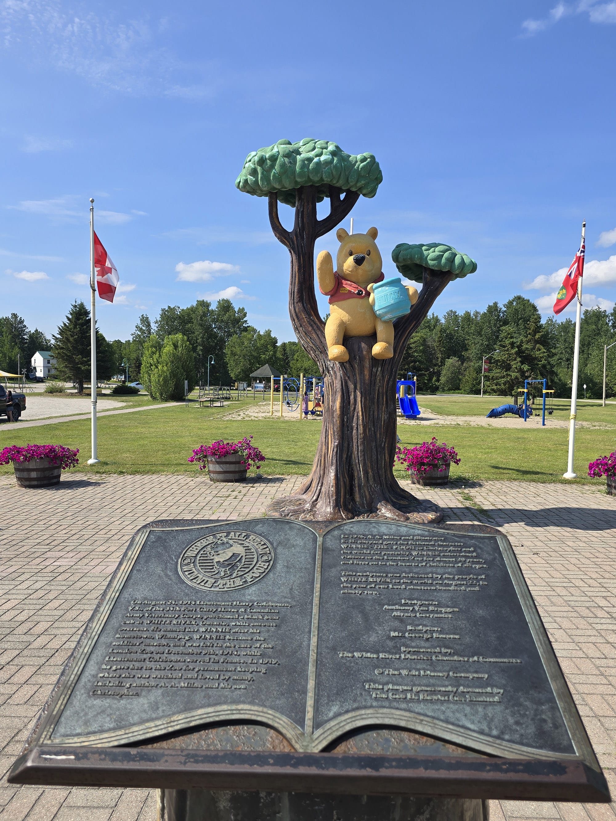 A statue of Winnie the Pooh in a tree, with a memorial park behind it.