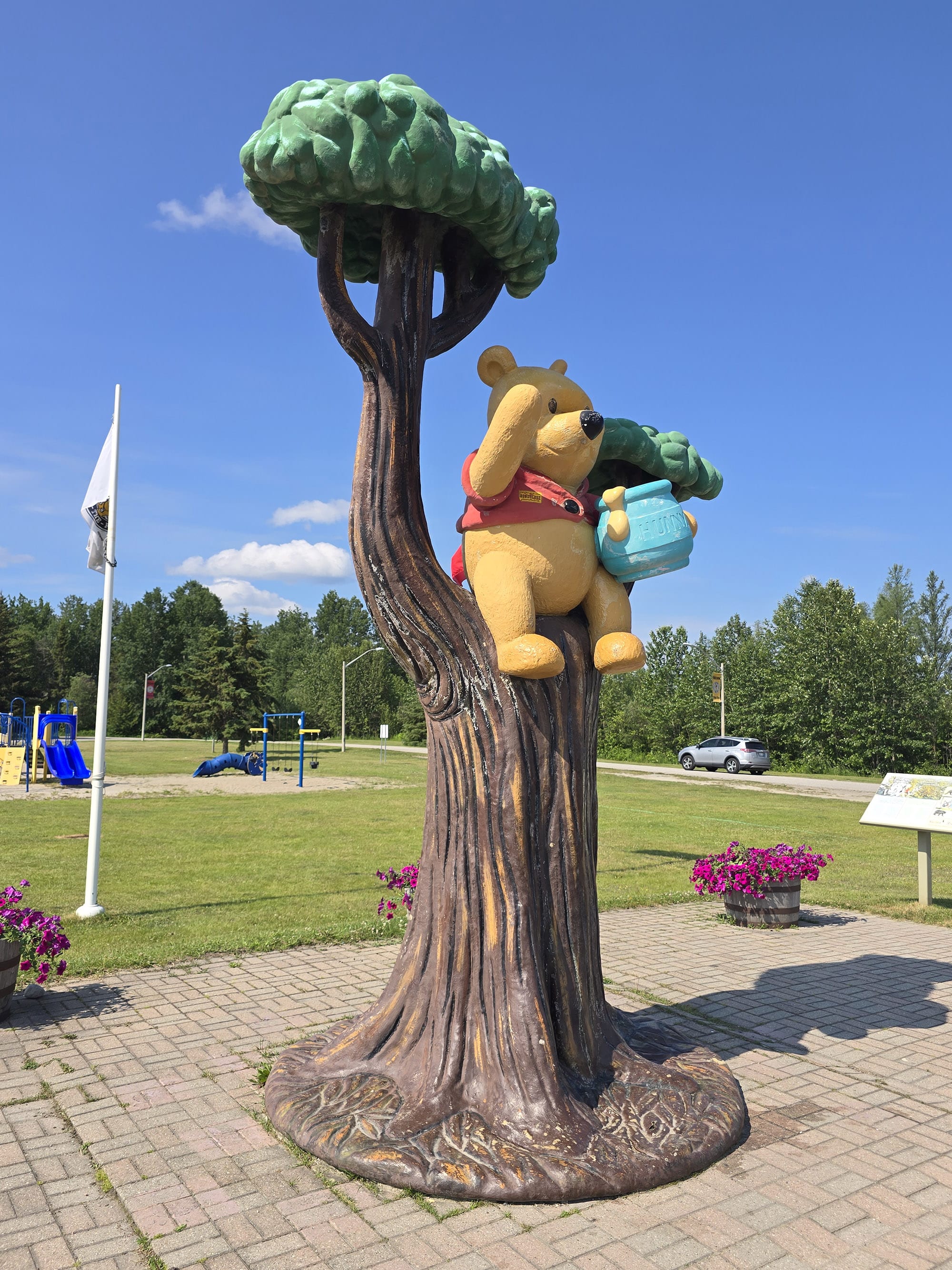A statue of Winnie the Pooh in a tree, with a memorial park behind it.