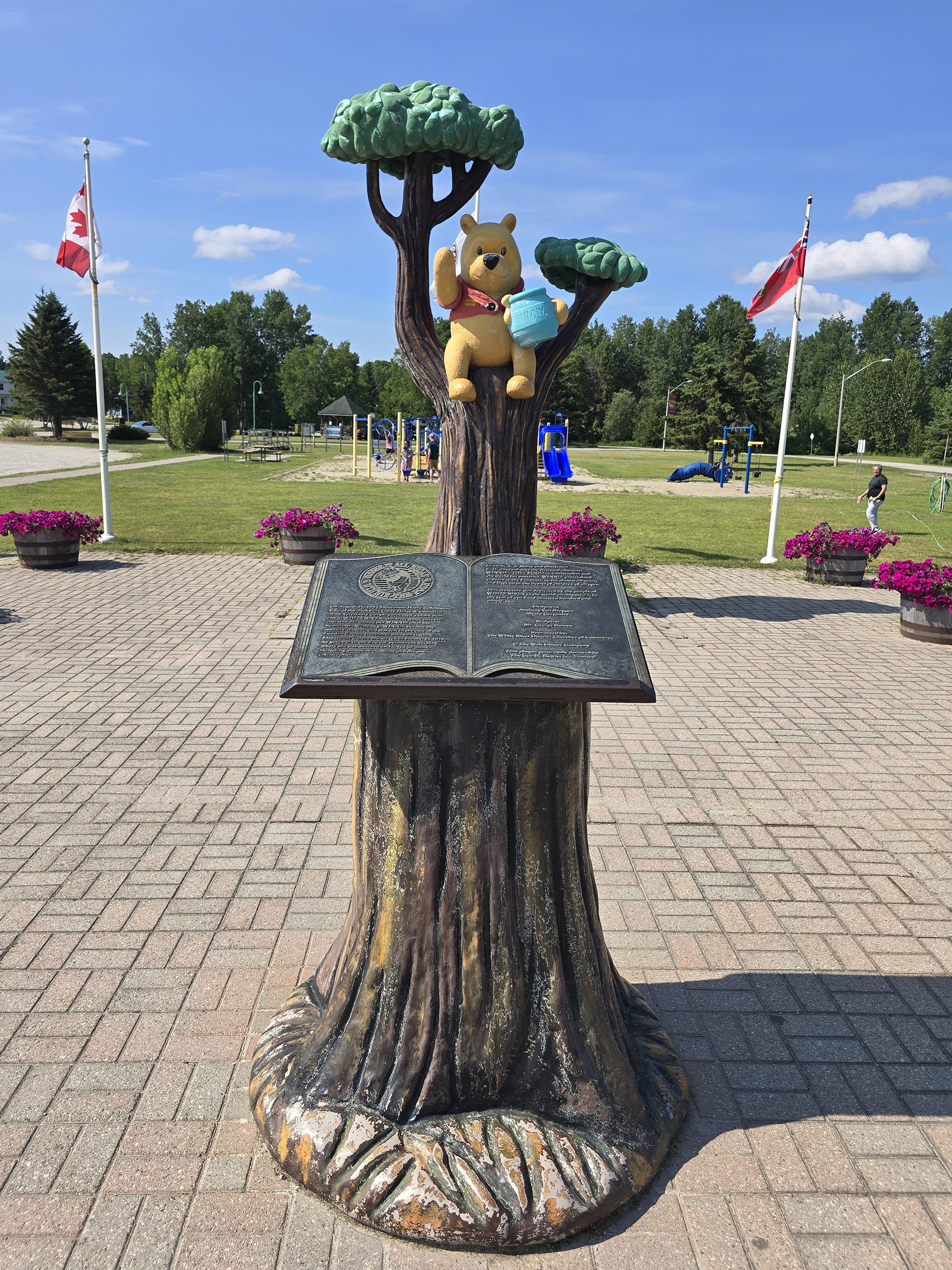 A statue of Winnie the Pooh in a tree, with a memorial park behind it.