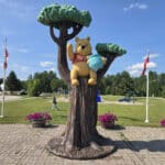A statue of Winnie the Pooh in a tree, with a memorial park behind it.