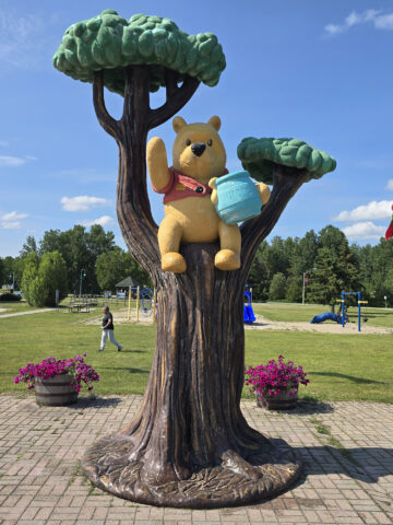 A statue of Winnie the Pooh in a tree, with a memorial park behind it.
