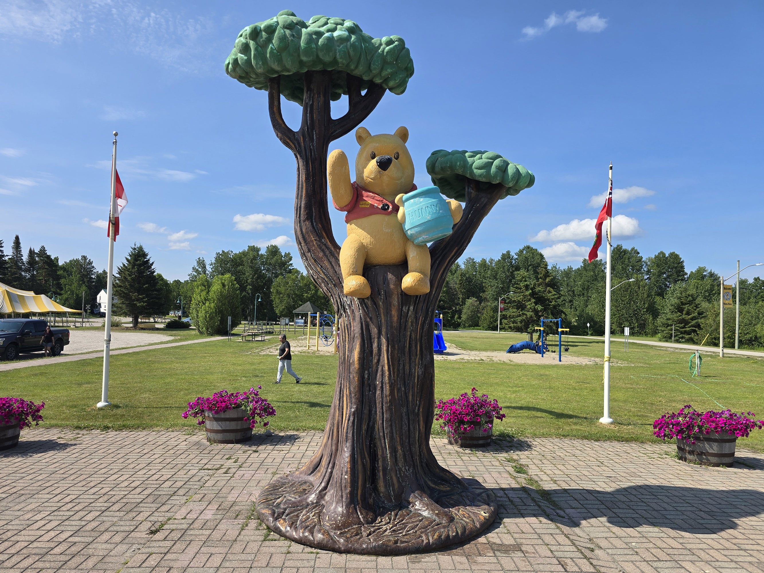 A statue of Winnie the Pooh in a tree, with a memorial park behind it.