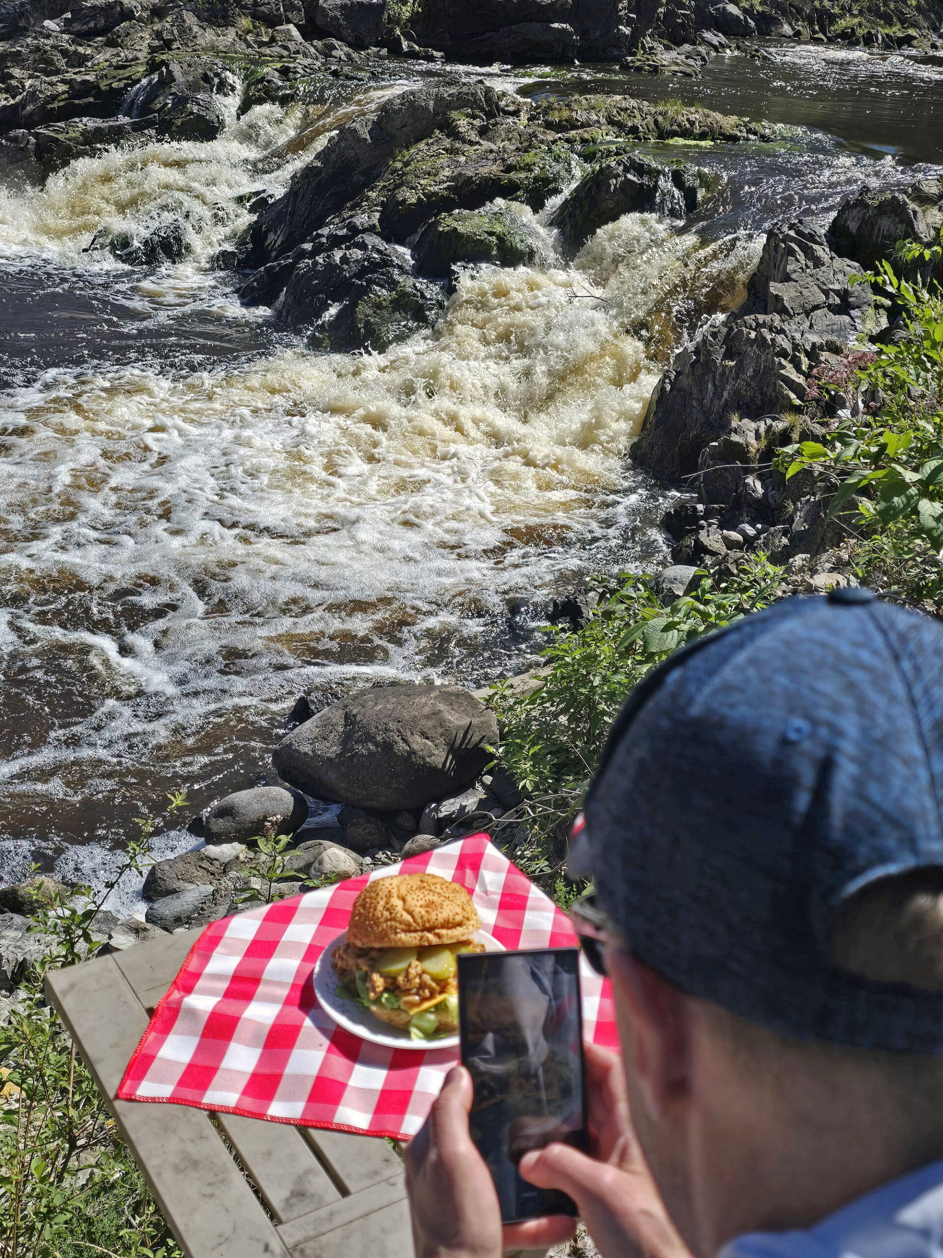 A man photographing big mac sloppy joes in front of a waterfall.