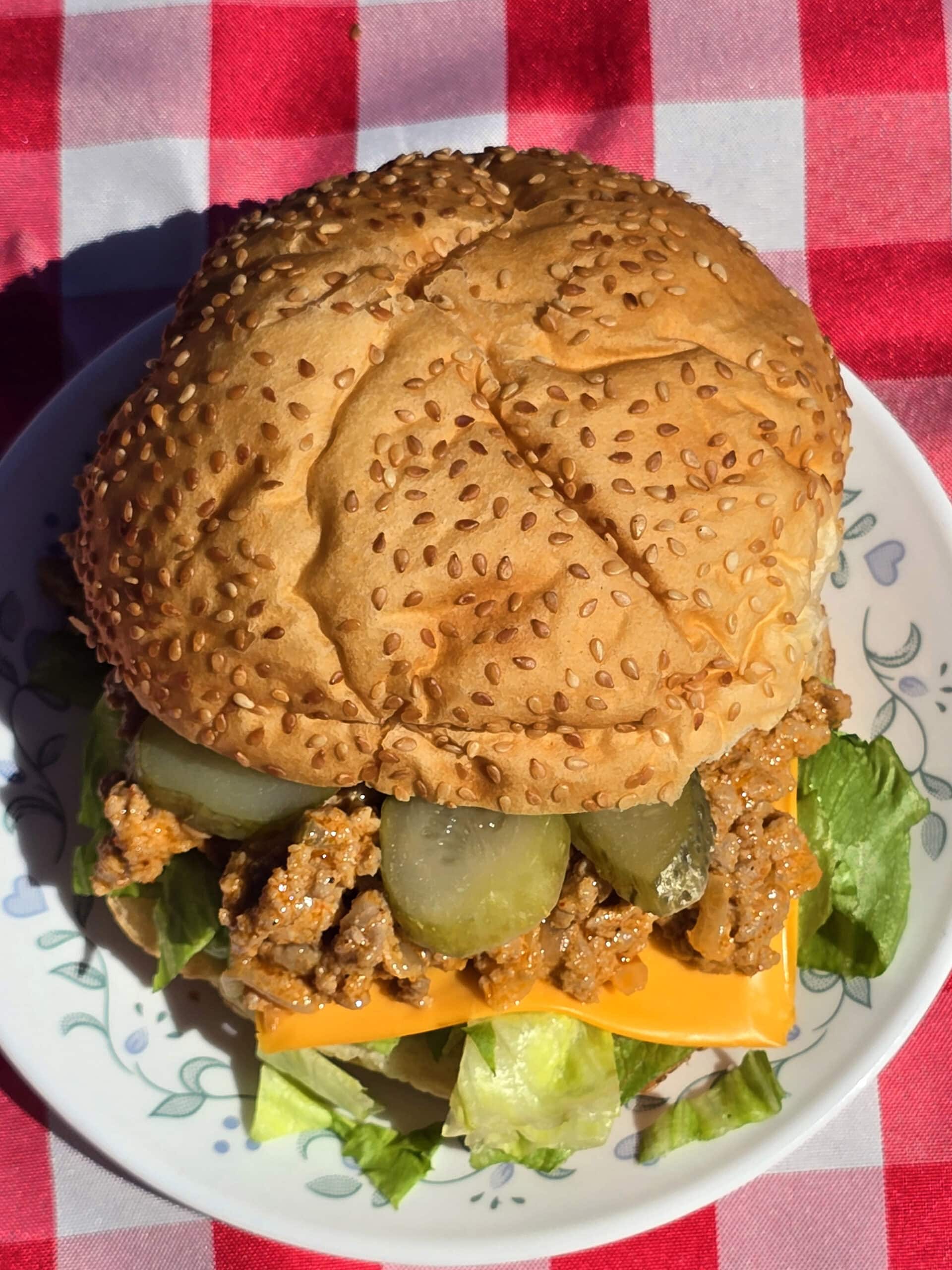A big mac sloppy joe sandwich on a plate, lettuce, pickles, and cheese are visible.