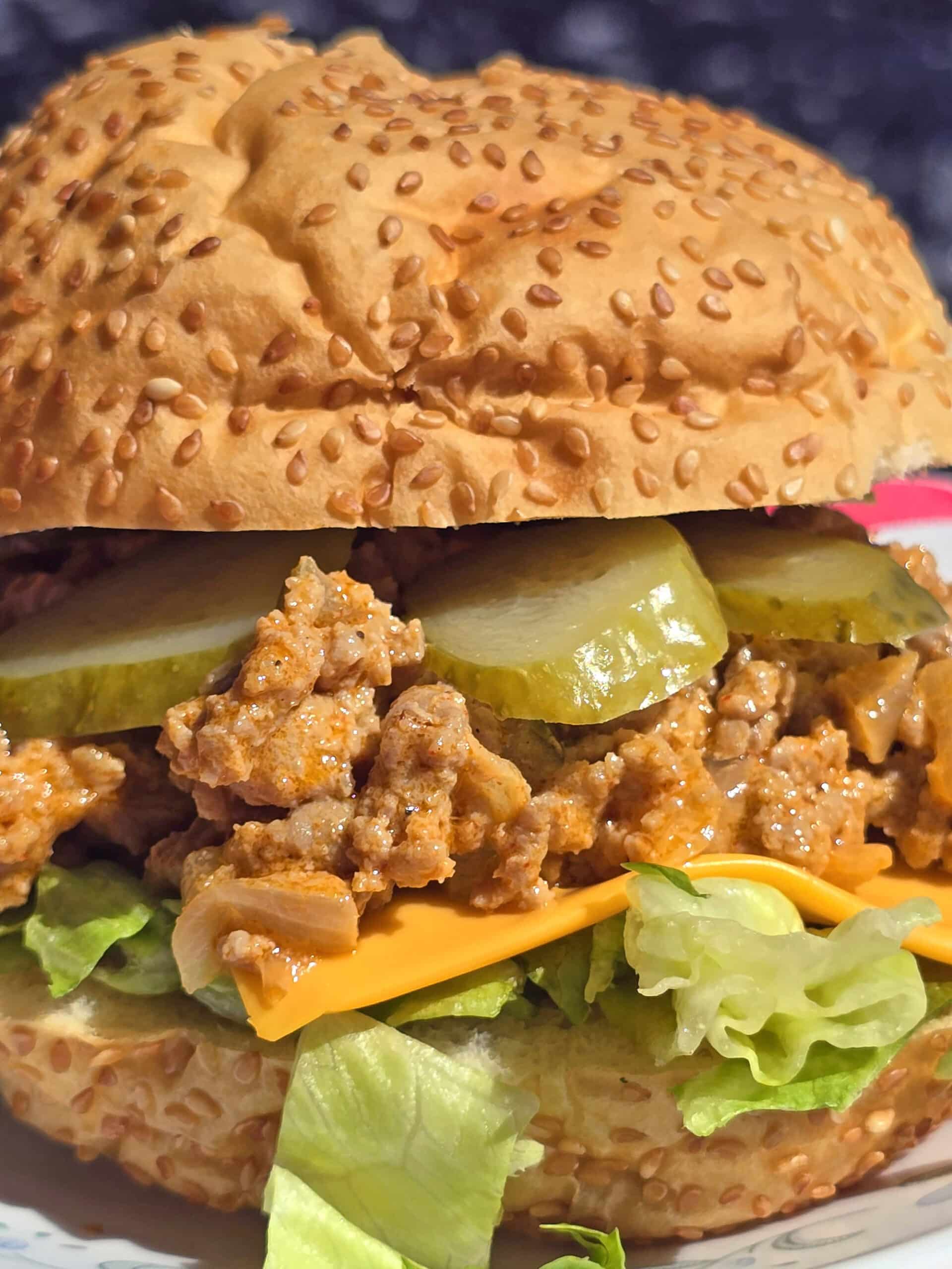 A big mac sloppy joe sandwich on a plate, lettuce, pickles, and cheese are visible.