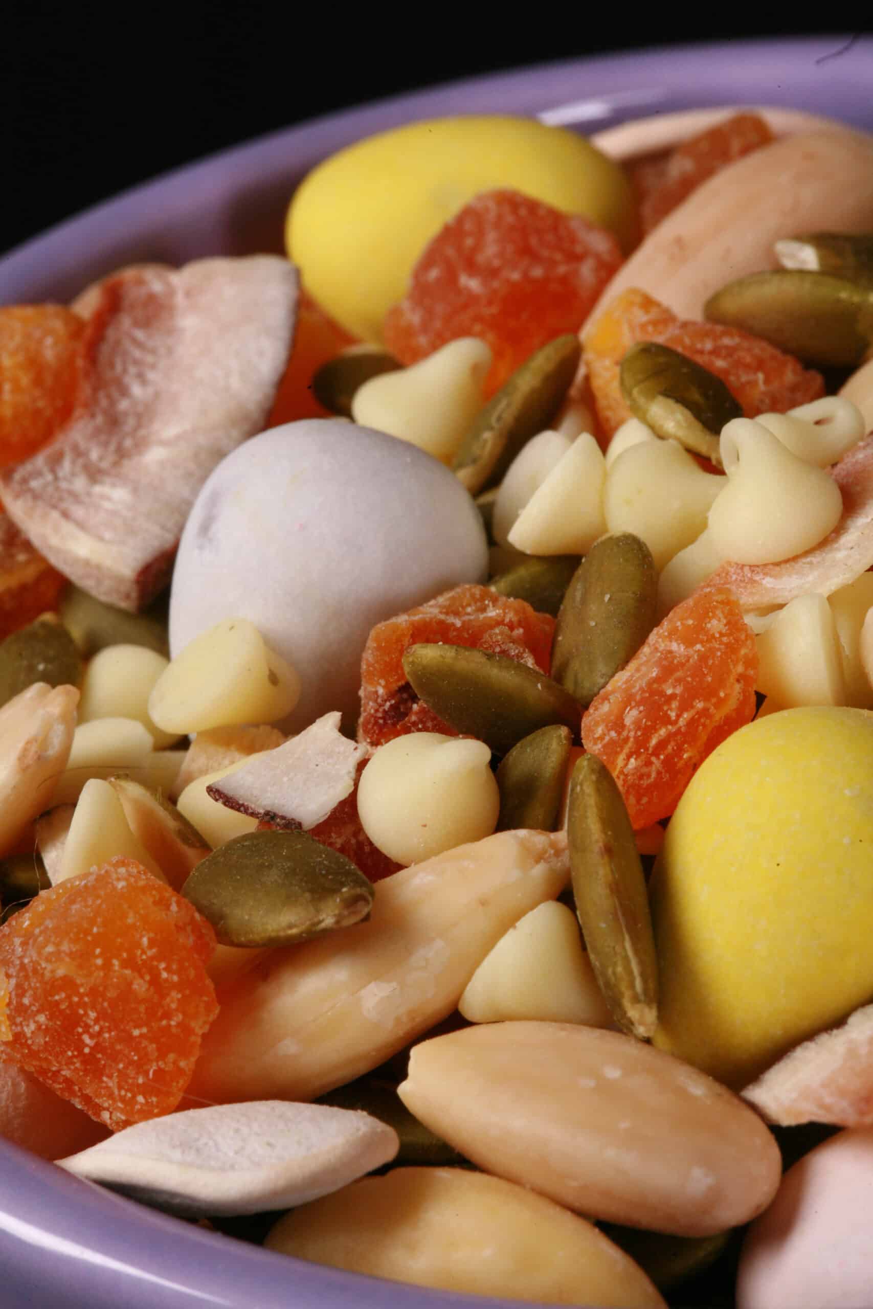 A bowl of Easter trail mix, with coconut, apricot, pumpkin seeds, pepitas, which chocolate, and mini eggs.