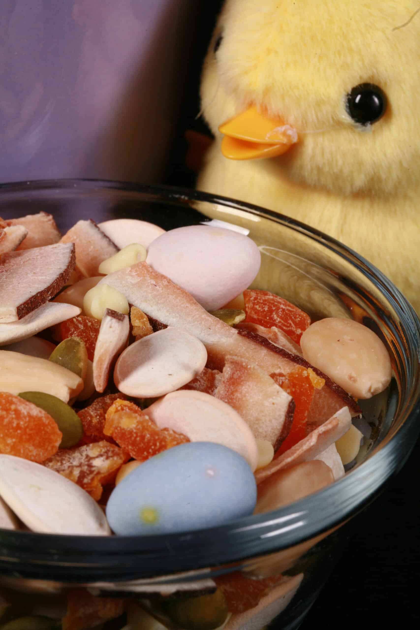 2 bowls of Easter trail mix, with coconut, apricot, pumpkin seeds, pepitas, which chocolate, and mini eggs. There is a toy chick next to them.
