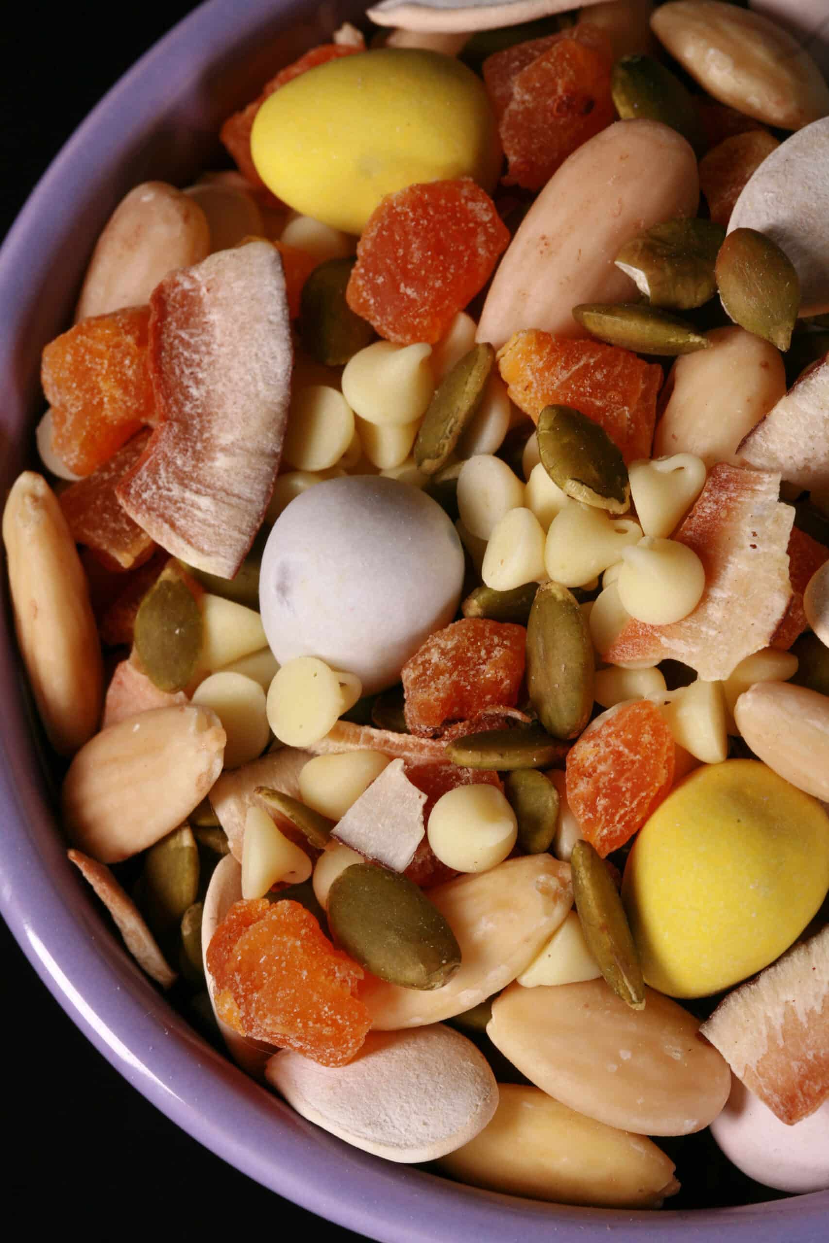 A bowl of Easter trail mix, with coconut, apricot, pumpkin seeds, pepitas, which chocolate, and mini eggs.