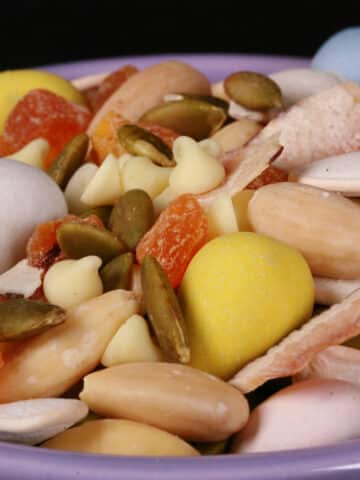 A bowl of Easter trail mix, with coconut, apricot, pumpkin seeds, pepitas, which chocolate, and mini eggs.