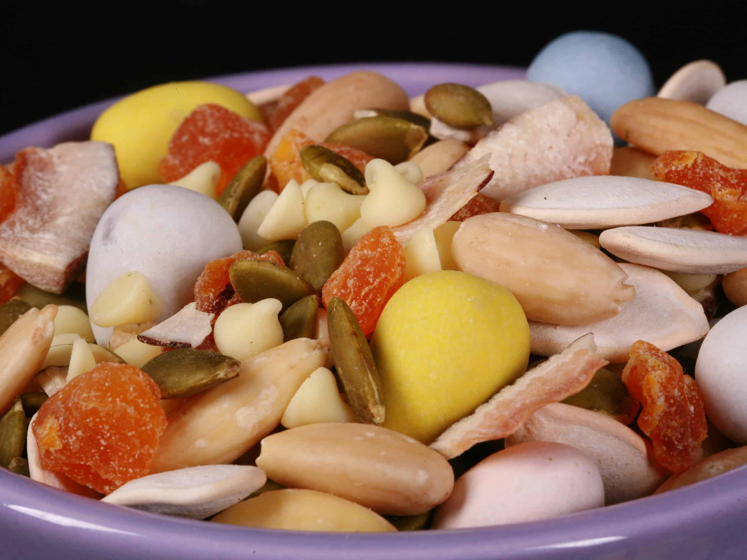 A bowl of Easter trail mix, with coconut, apricot, pumpkin seeds, pepitas, which chocolate, and mini eggs.