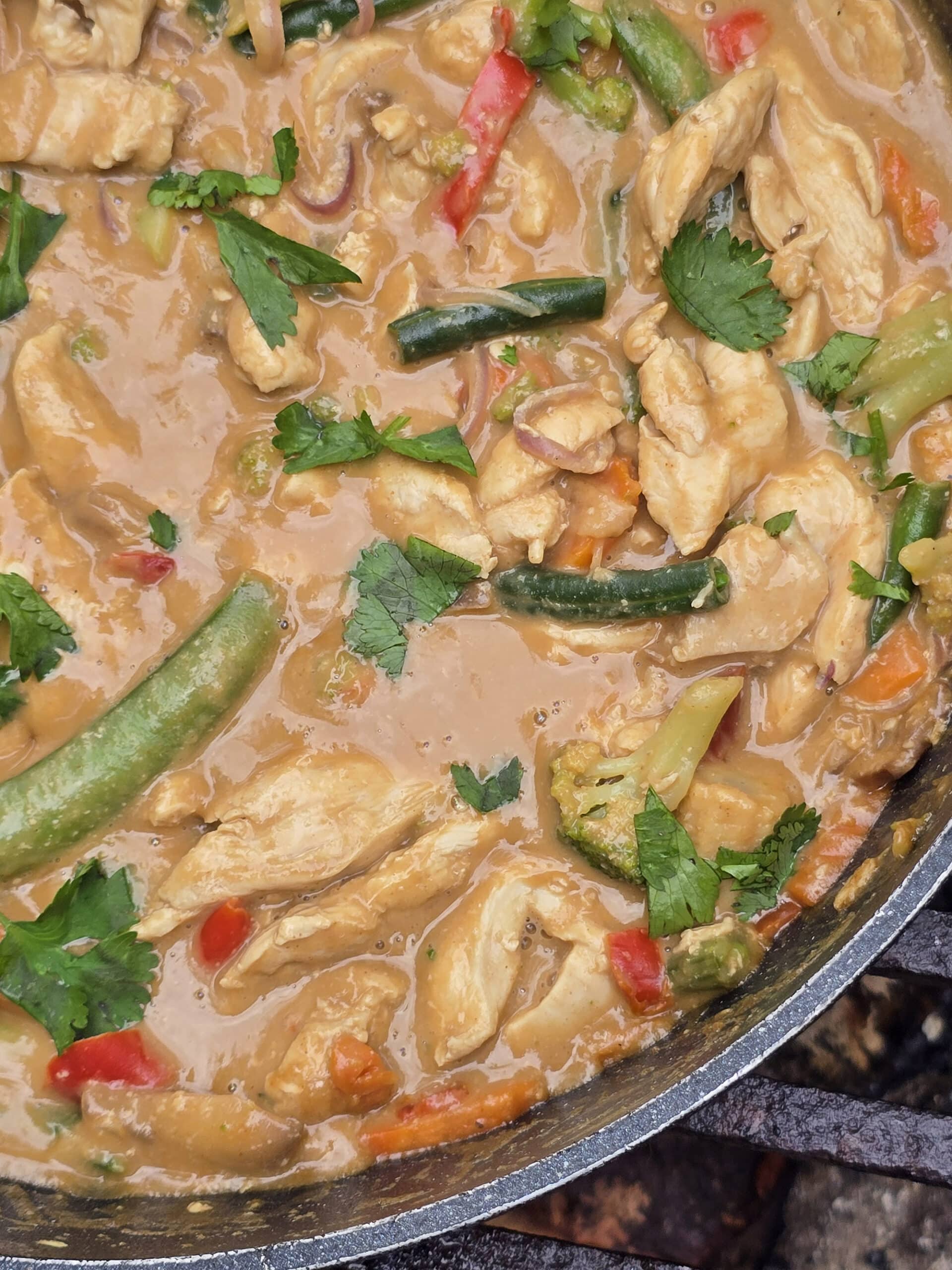 A pan of peanut chicken stir fry with a variety of colourful vegetables in it.