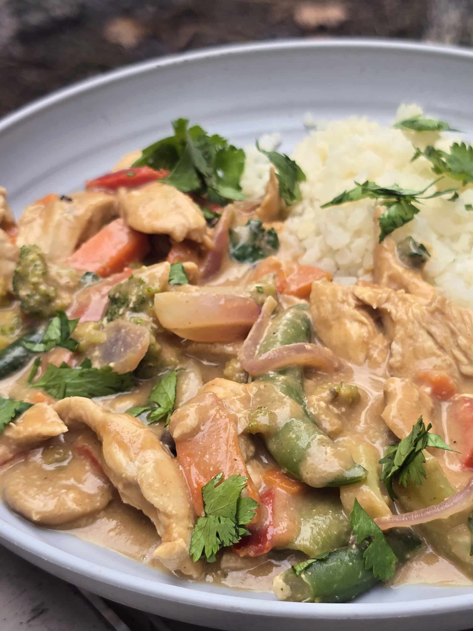 A plate of peanut chicken stir fry with a variety of colourful vegetables in it.