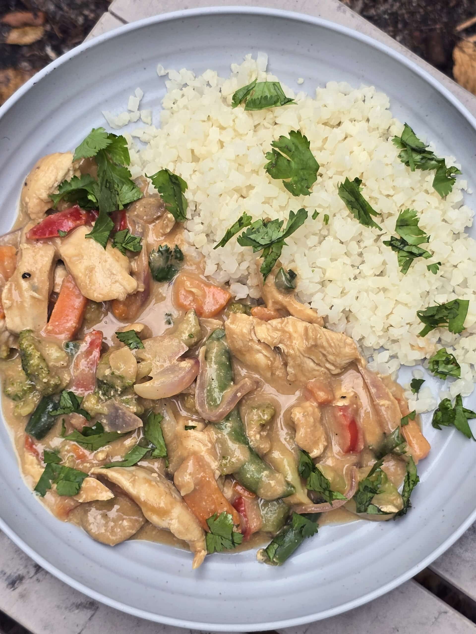 A plate of peanut chicken stir fry with a variety of colourful vegetables in it.