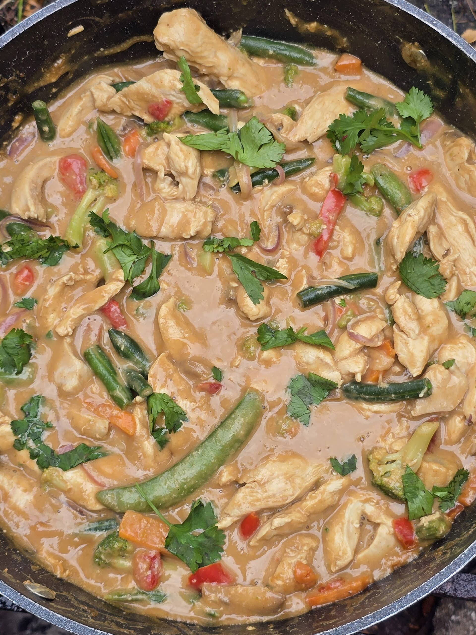 A pan of peanut chicken stir fry with a variety of colourful vegetables in it.