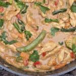 A pan of peanut chicken stir fry with a variety of colourful vegetables in it.