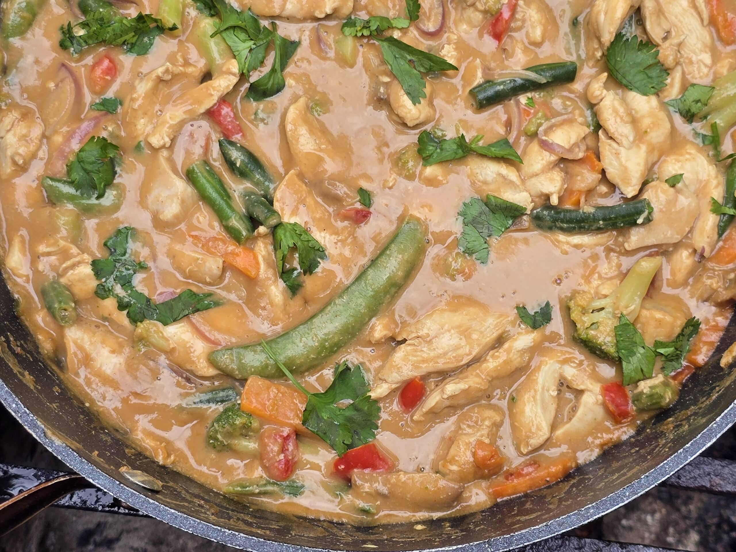A pan of peanut chicken stir fry with a variety of colourful vegetables in it.