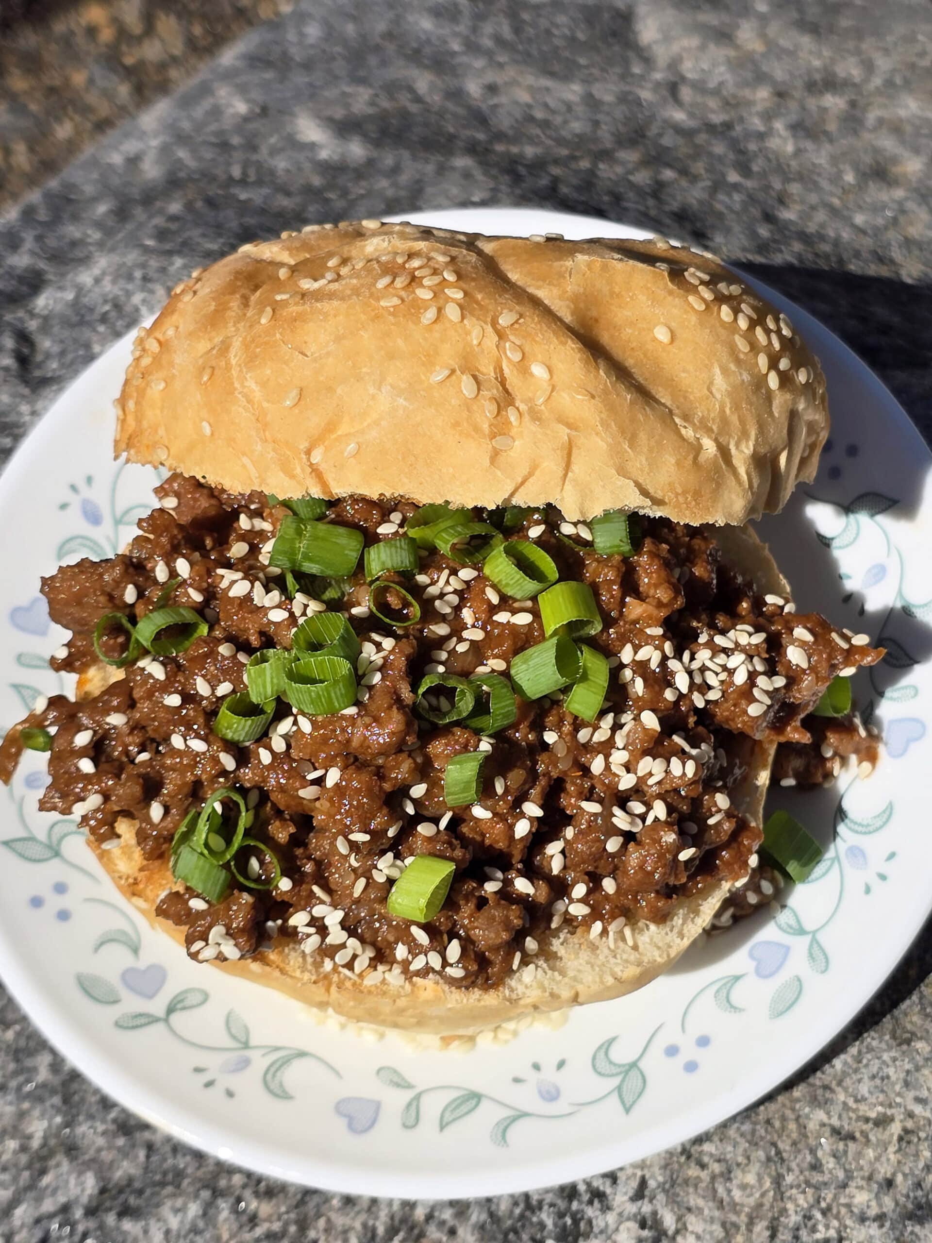 A Korean BBQ Sloppy Joes sandwich with green onions and sesame seeds.