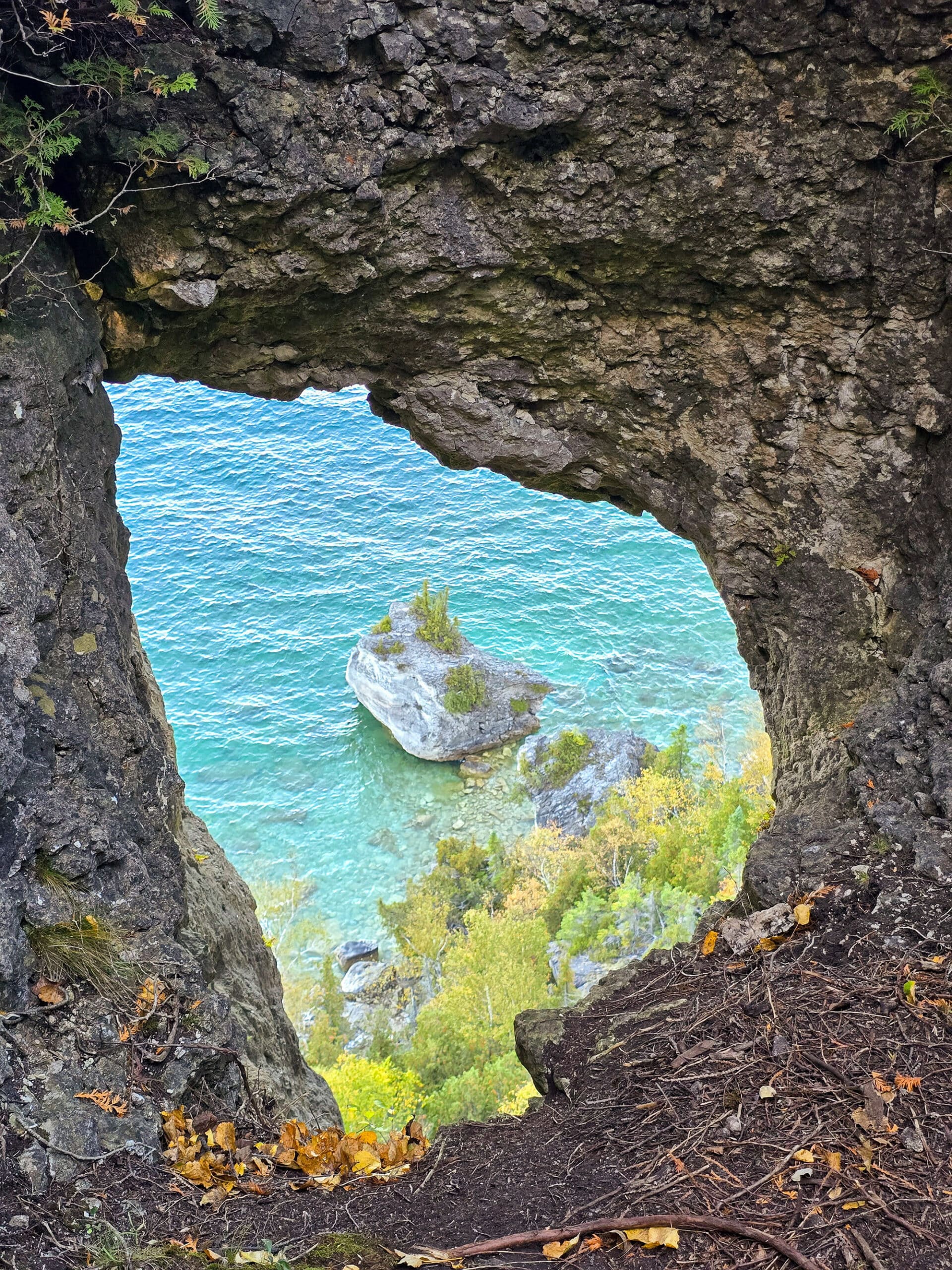 A rock face with a large hole in it, looking down over turquoise water below.