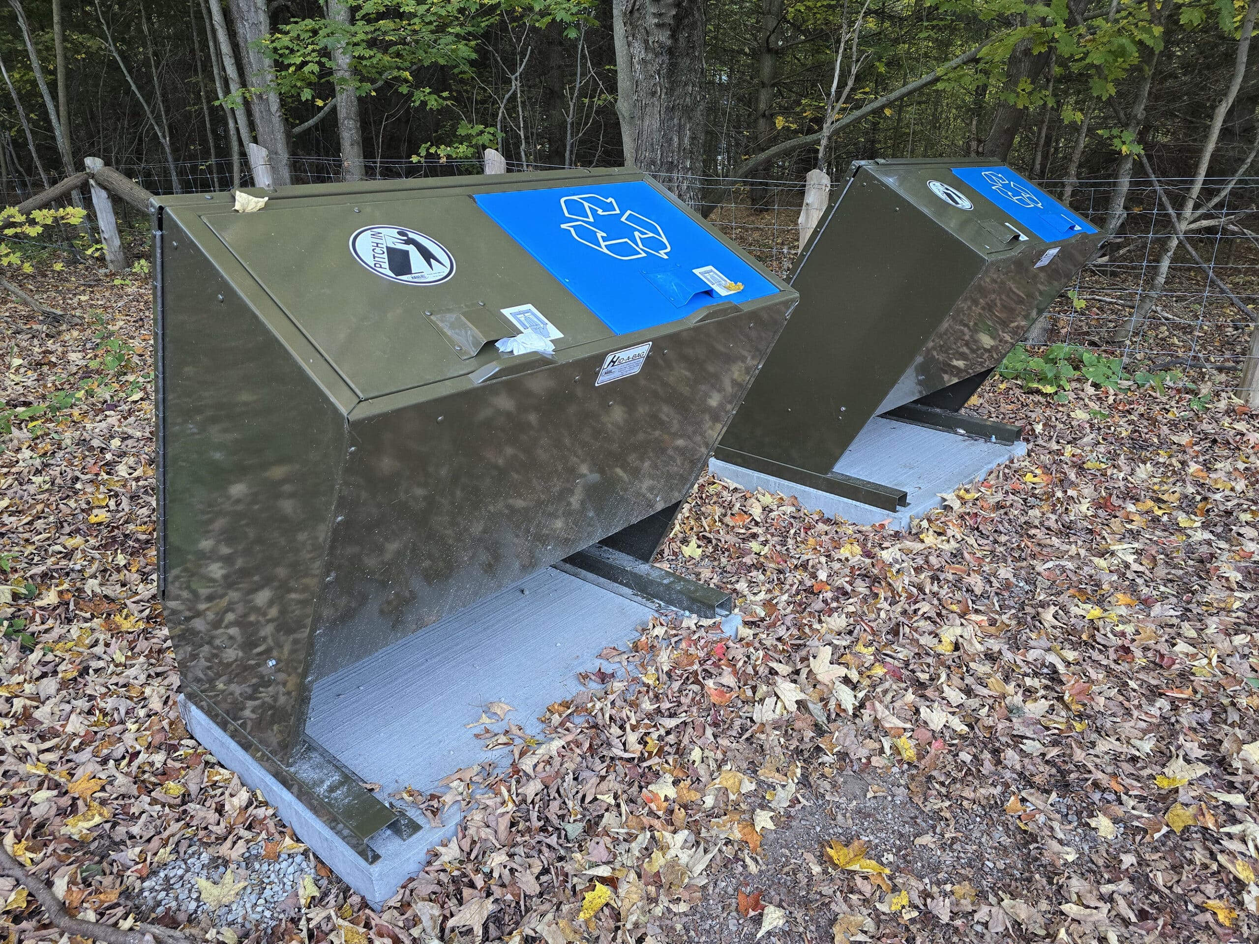 2 garbage and recycling receptacles in a parking lot.