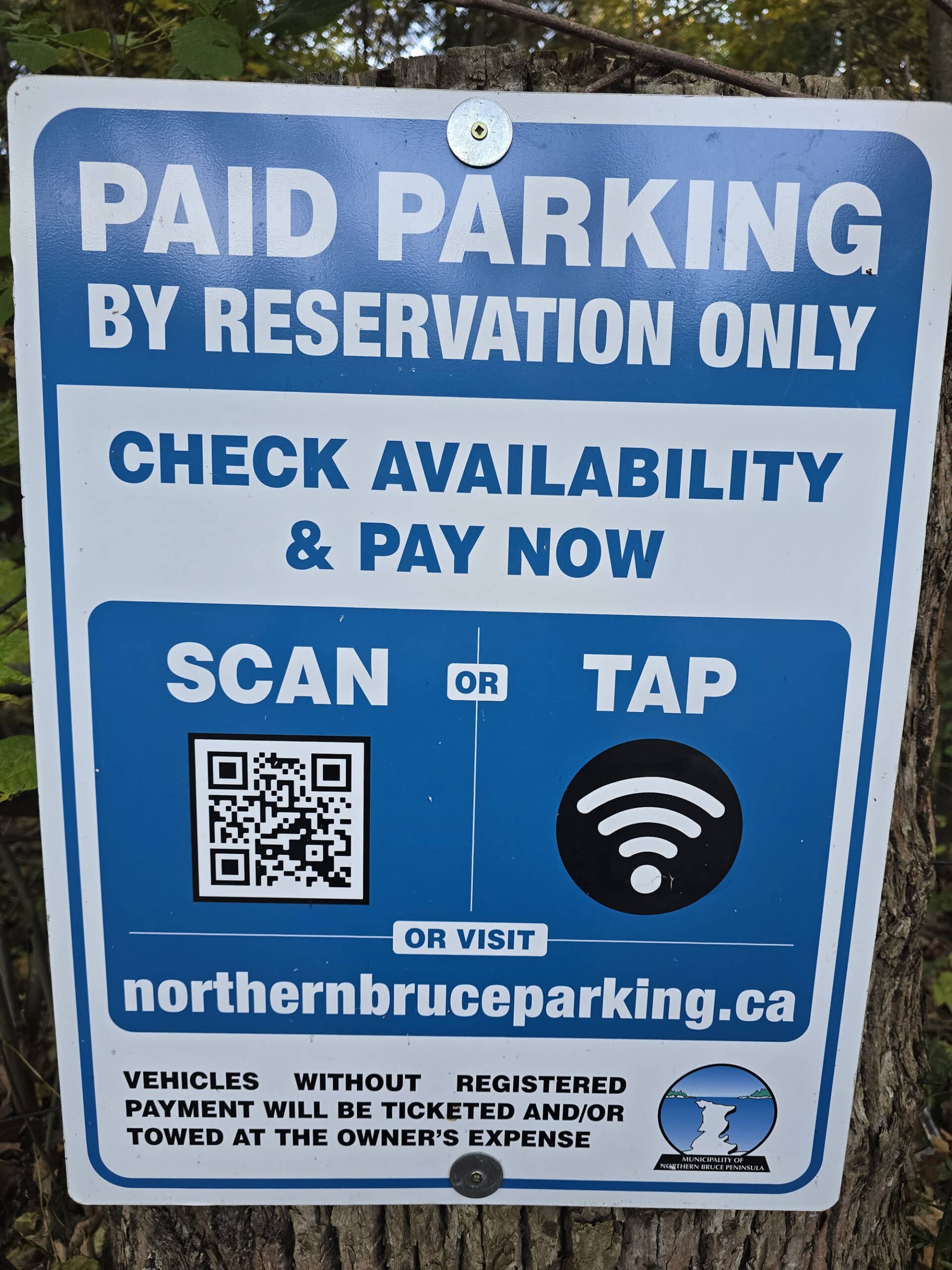 A parking sign that says by reservation only, inviting visitors to scan or tap to pay.