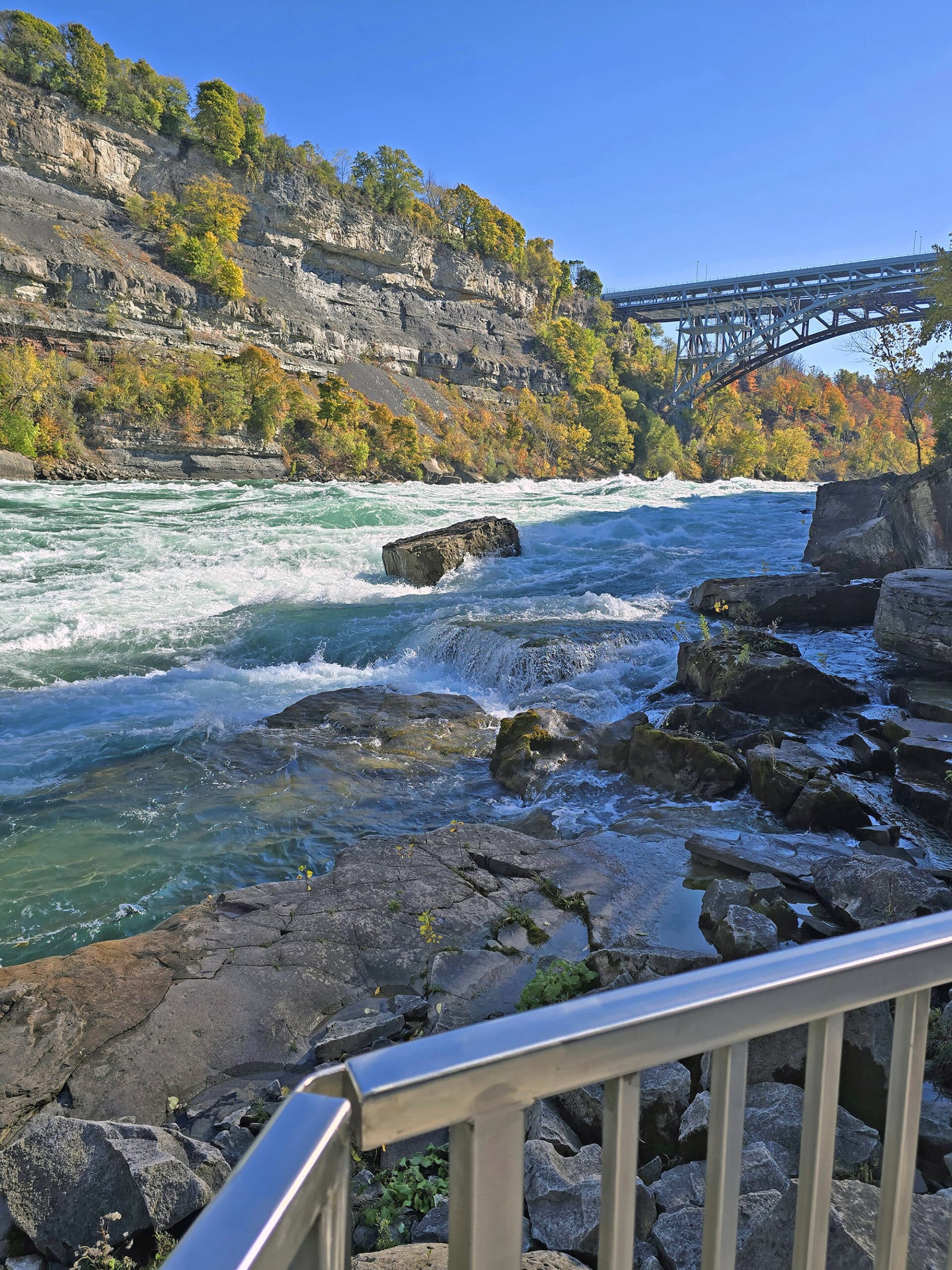 Looking out over white water rapids from the boardwalk at white water walk, a bridge in the background.