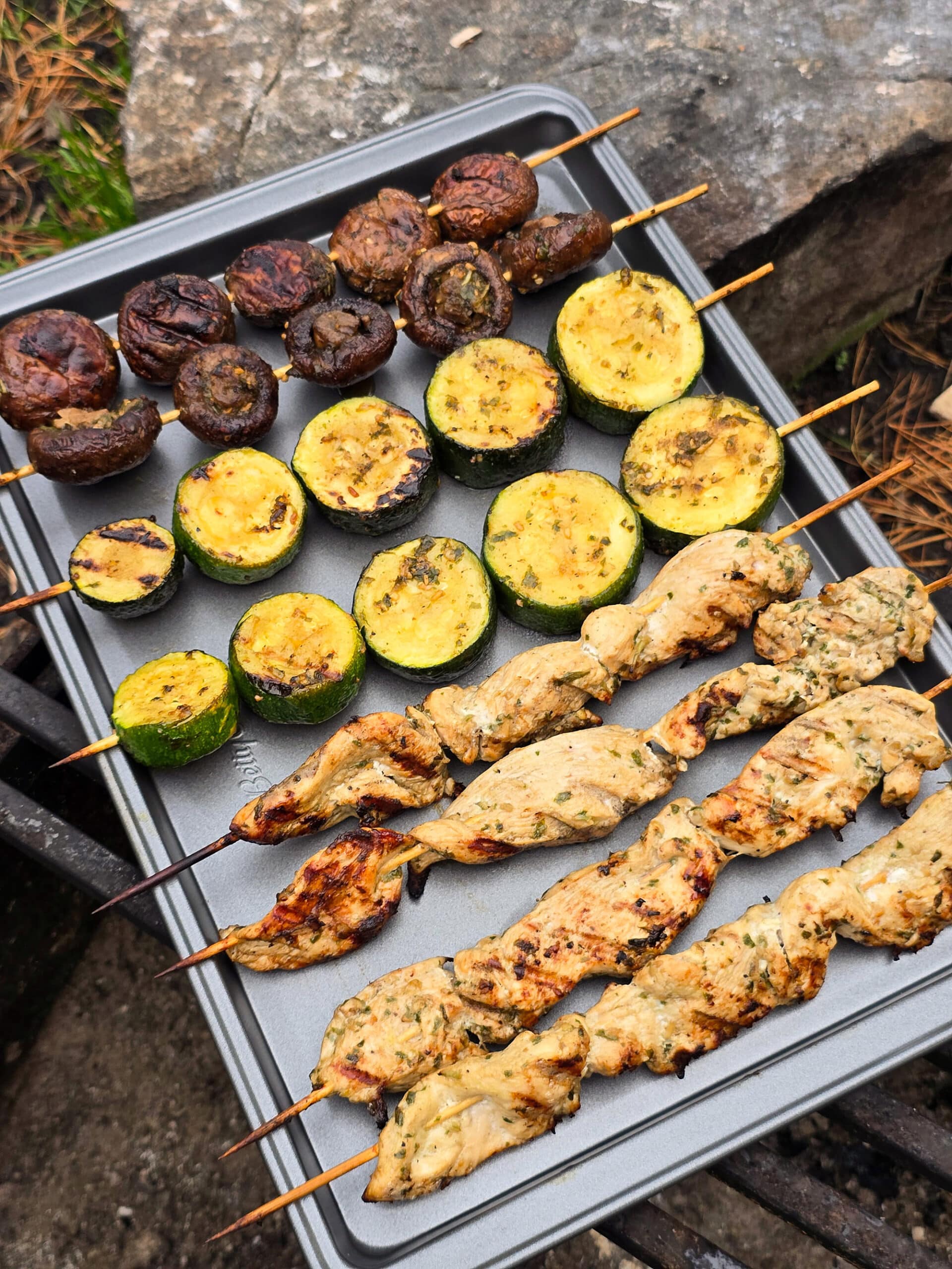 Individual skewers of pesto mushrooms and zucchini slices on a pan with pesto chicken skewers.
