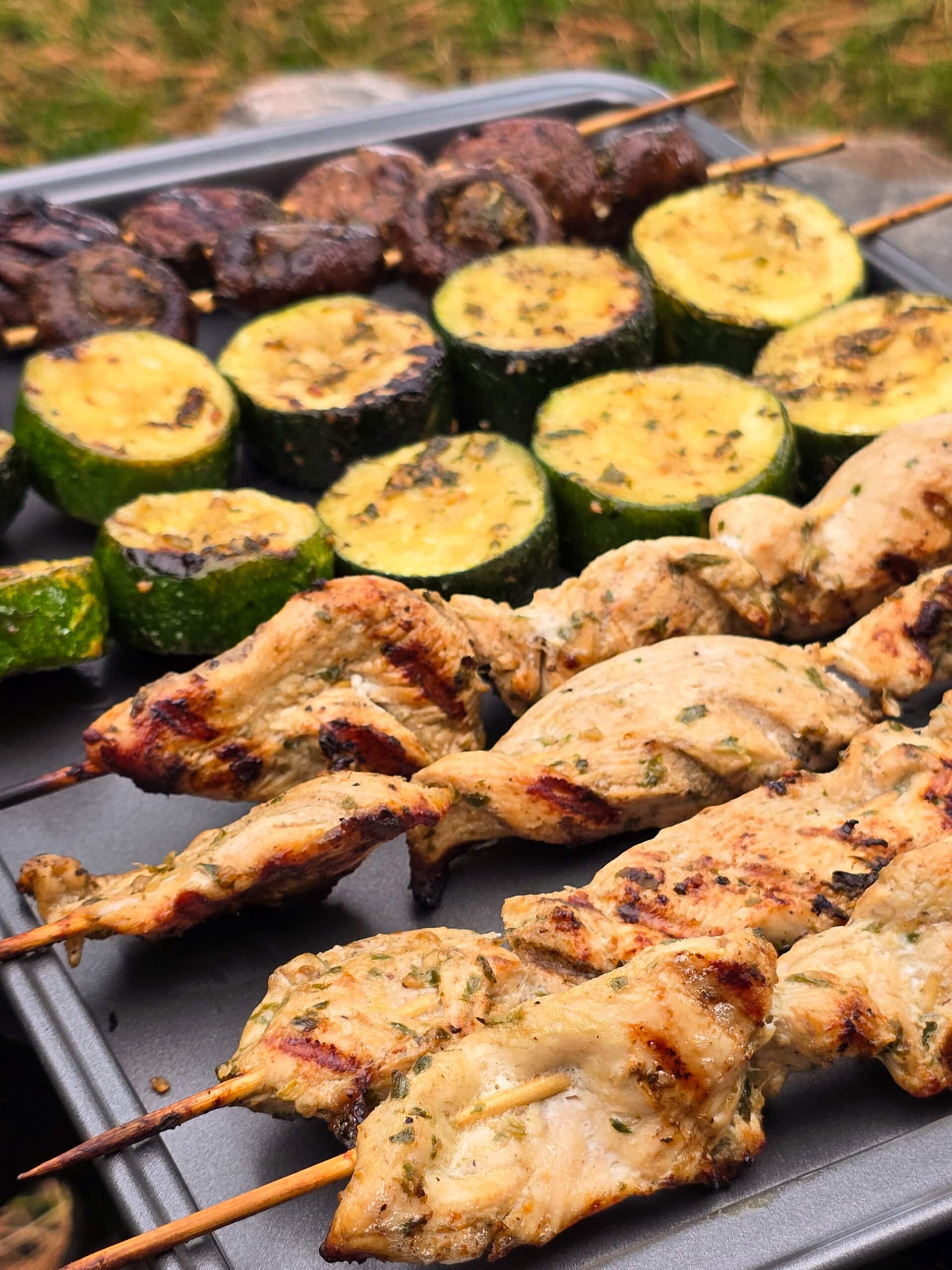 Individual skewers of pesto mushrooms and zucchini slices on a pan with pesto chicken skewers.