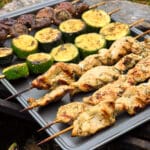 Individual skewers of pesto mushrooms and zucchini slices on a pan with pesto chicken skewers.