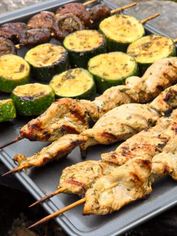 Individual skewers of pesto mushrooms and zucchini slices on a pan with pesto chicken skewers.