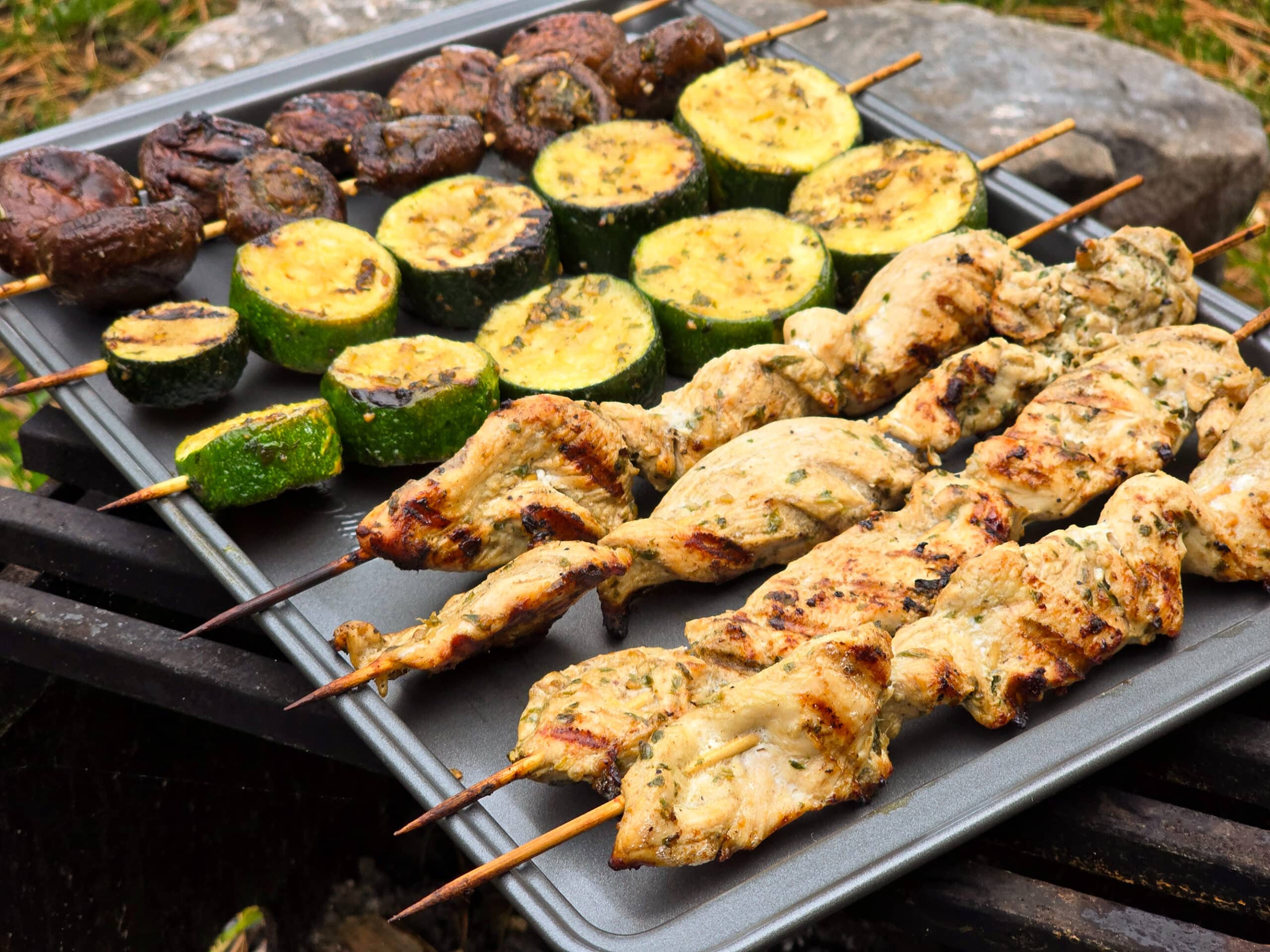 Individual skewers of pesto mushrooms and zucchini slices on a pan with pesto chicken skewers.